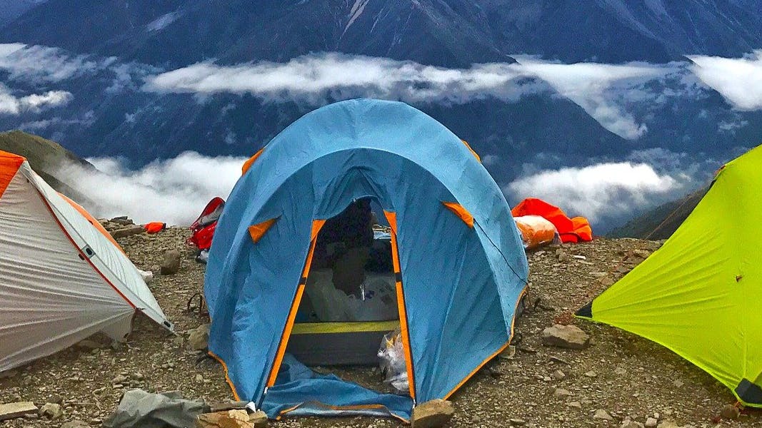 Three camping tents set up on a mountain at high elevation with clouds visible in the distance