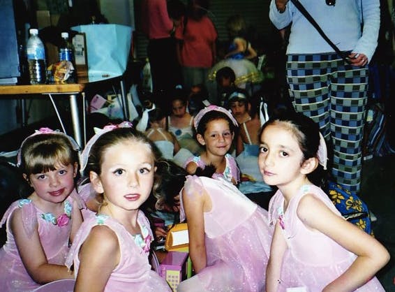 A group of young girls in ballerina outfits smile at the camera