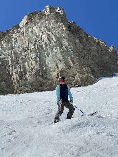 A girl standing under some rocks in snow on her skis.