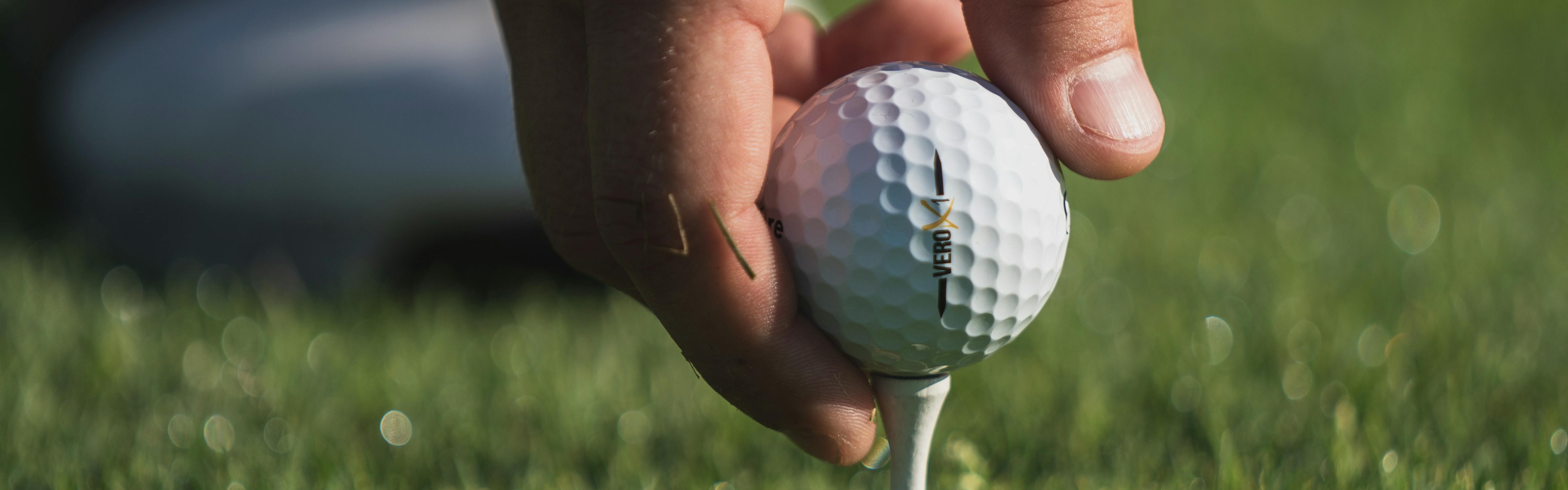 A man's hand places a golf ball onto a tee.