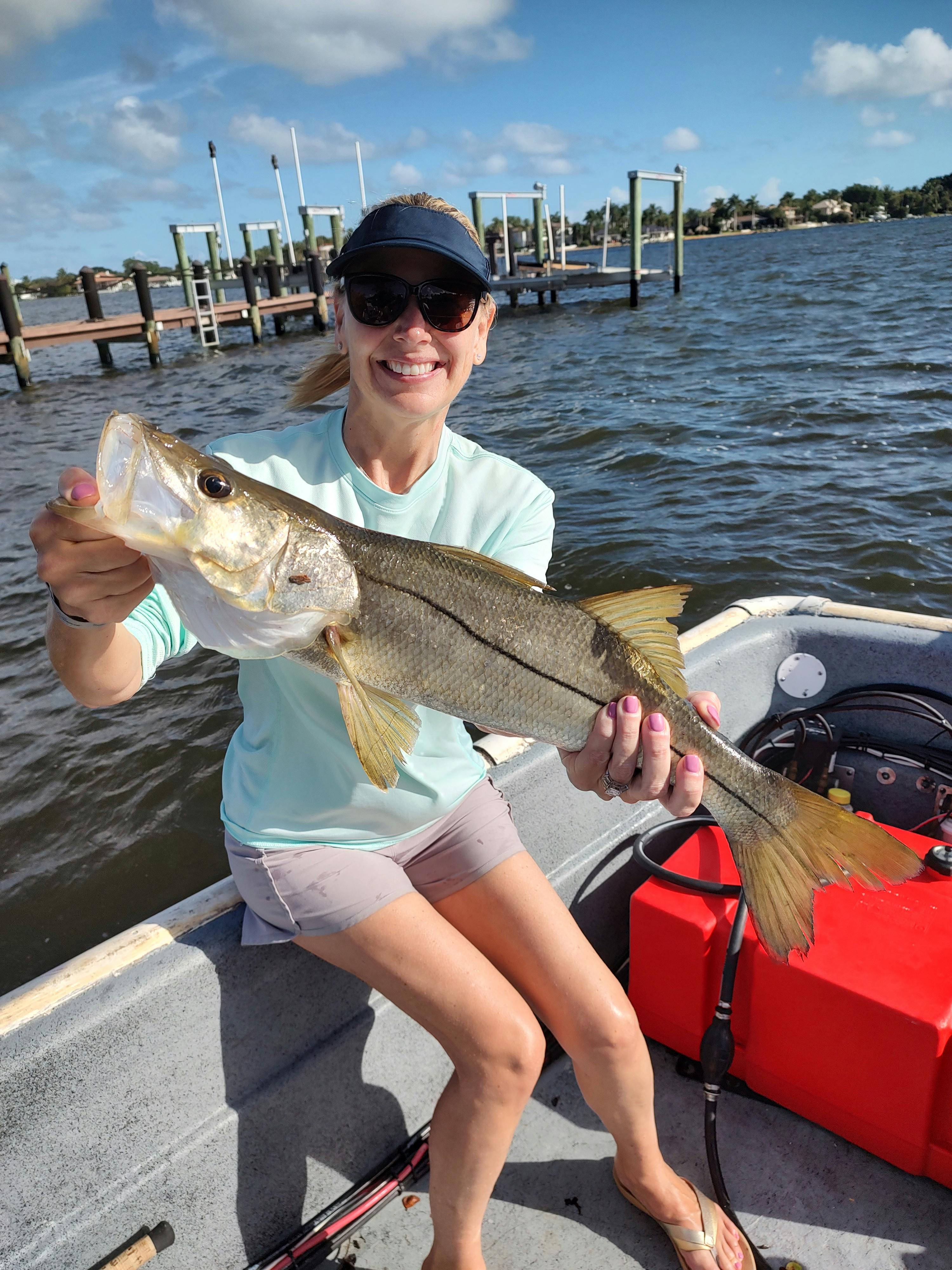A woman on a fishing boat holding a snook. 