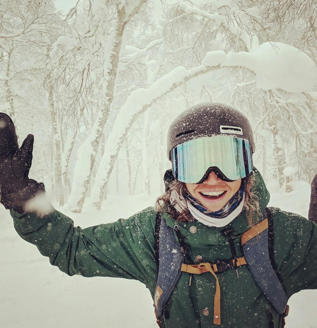 A snowboarder smiling and holding her hands up. She is wearing the Zeal Optics Beacon Goggles · 2021. 