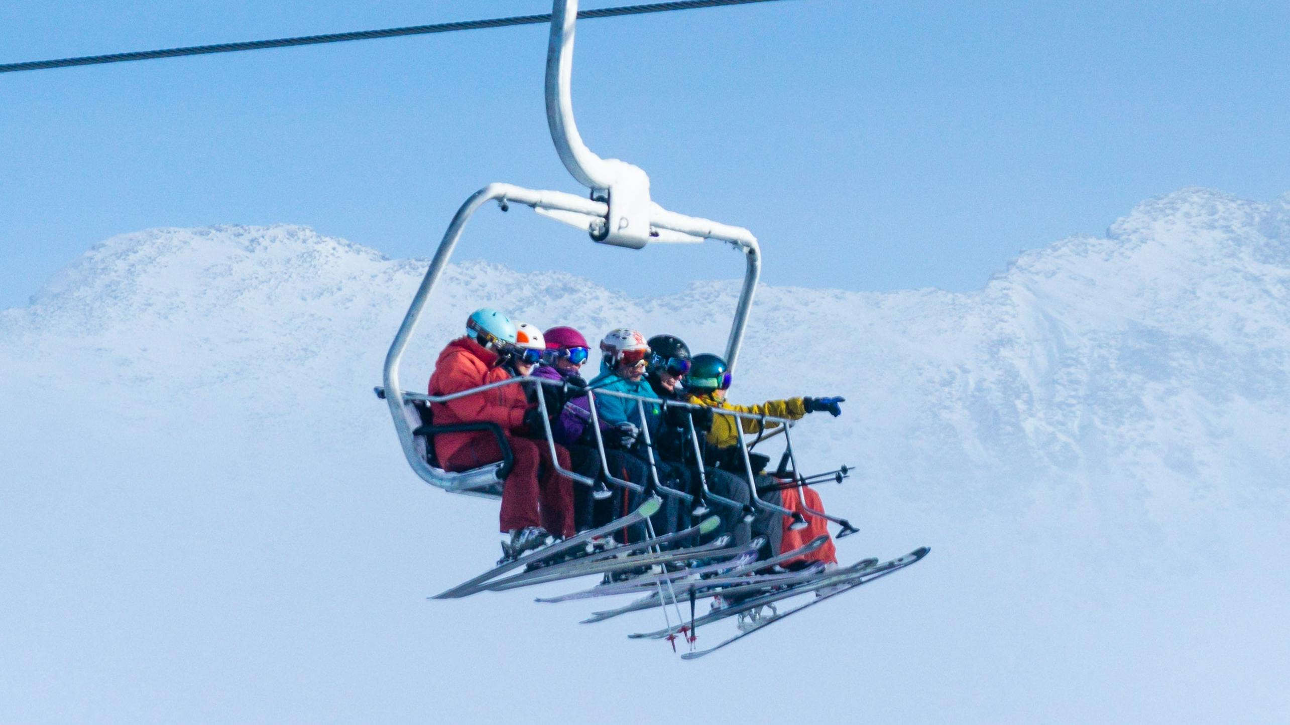 A family on a chairlift. They all have skis on and there is a snowy mountain in the background. 