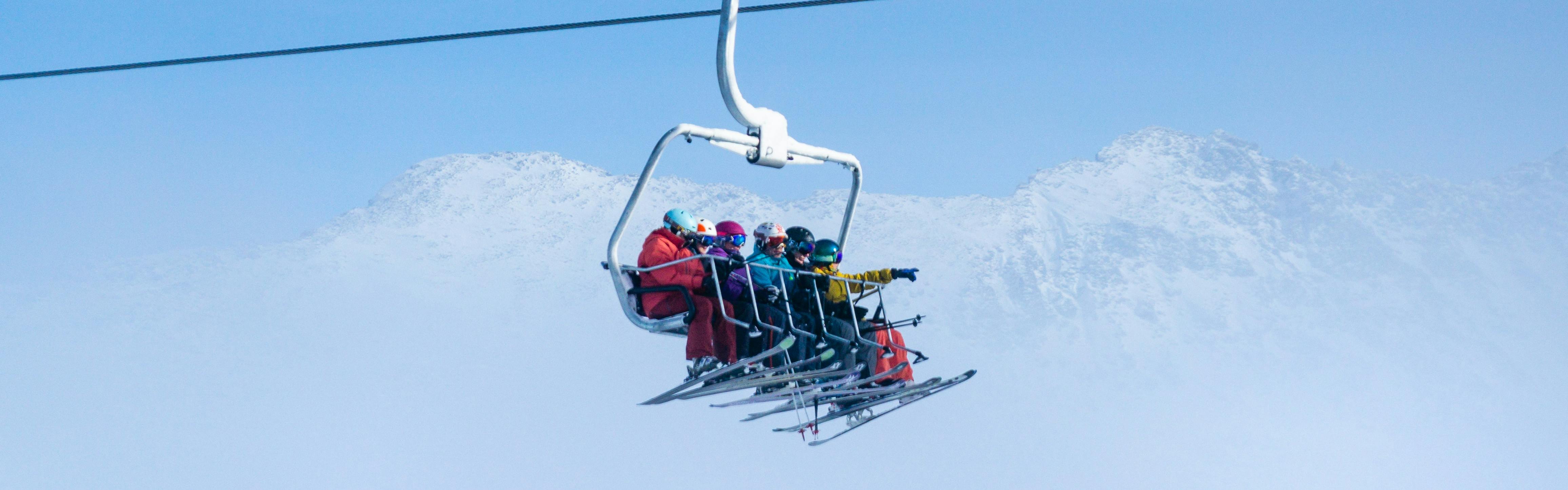 A family on a chairlift. They all have skis on and there is a snowy mountain in the background. 