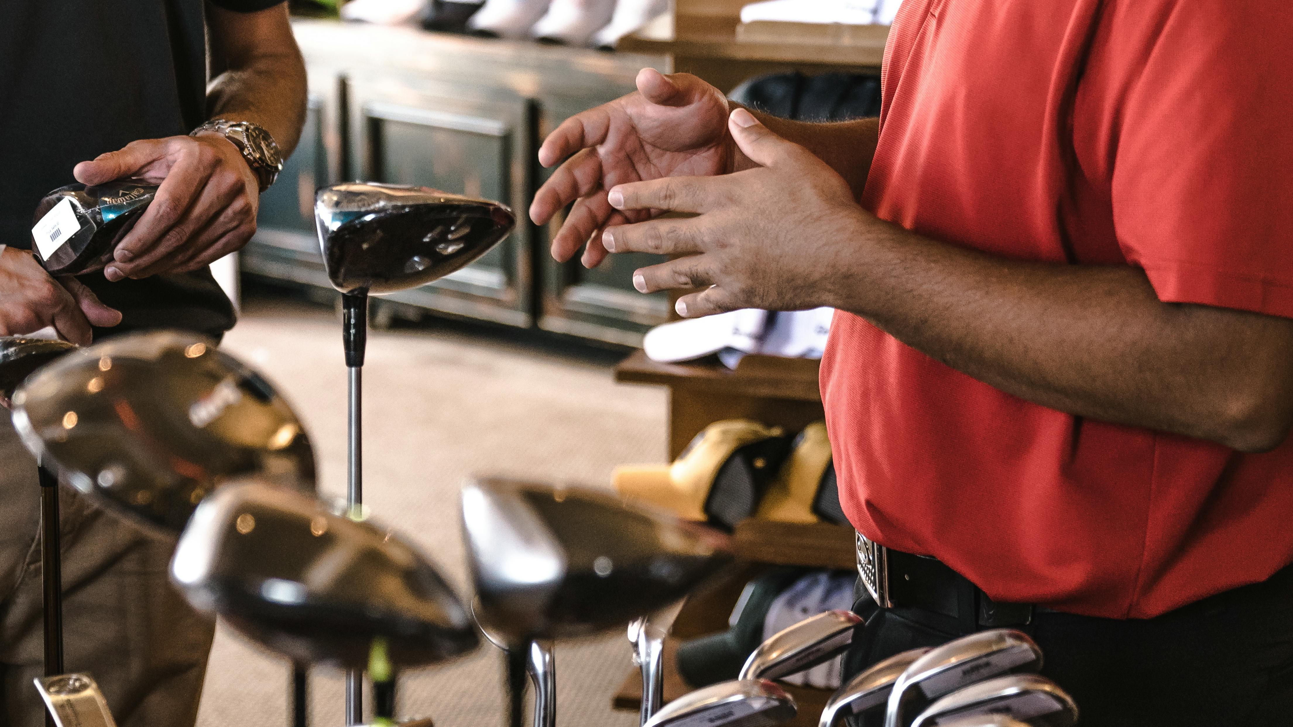 Two people in a golf store looking at different golf clubs. 