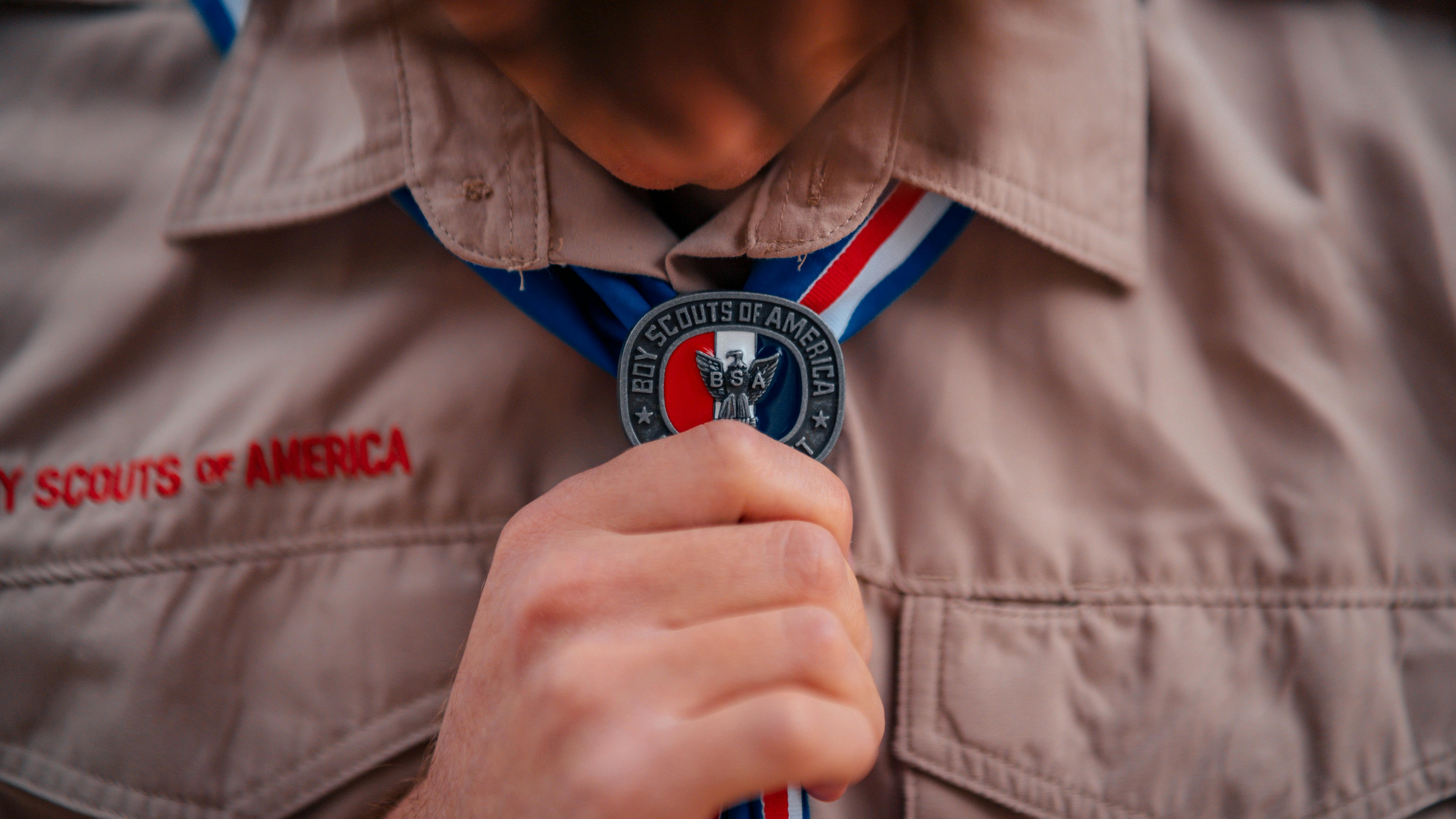A boy scout holds his medal while wearing his boy scout shirt.