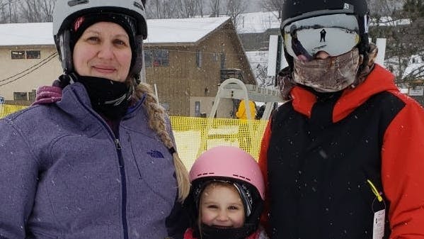 A mom and her two kids standing at the base of a ski resort.