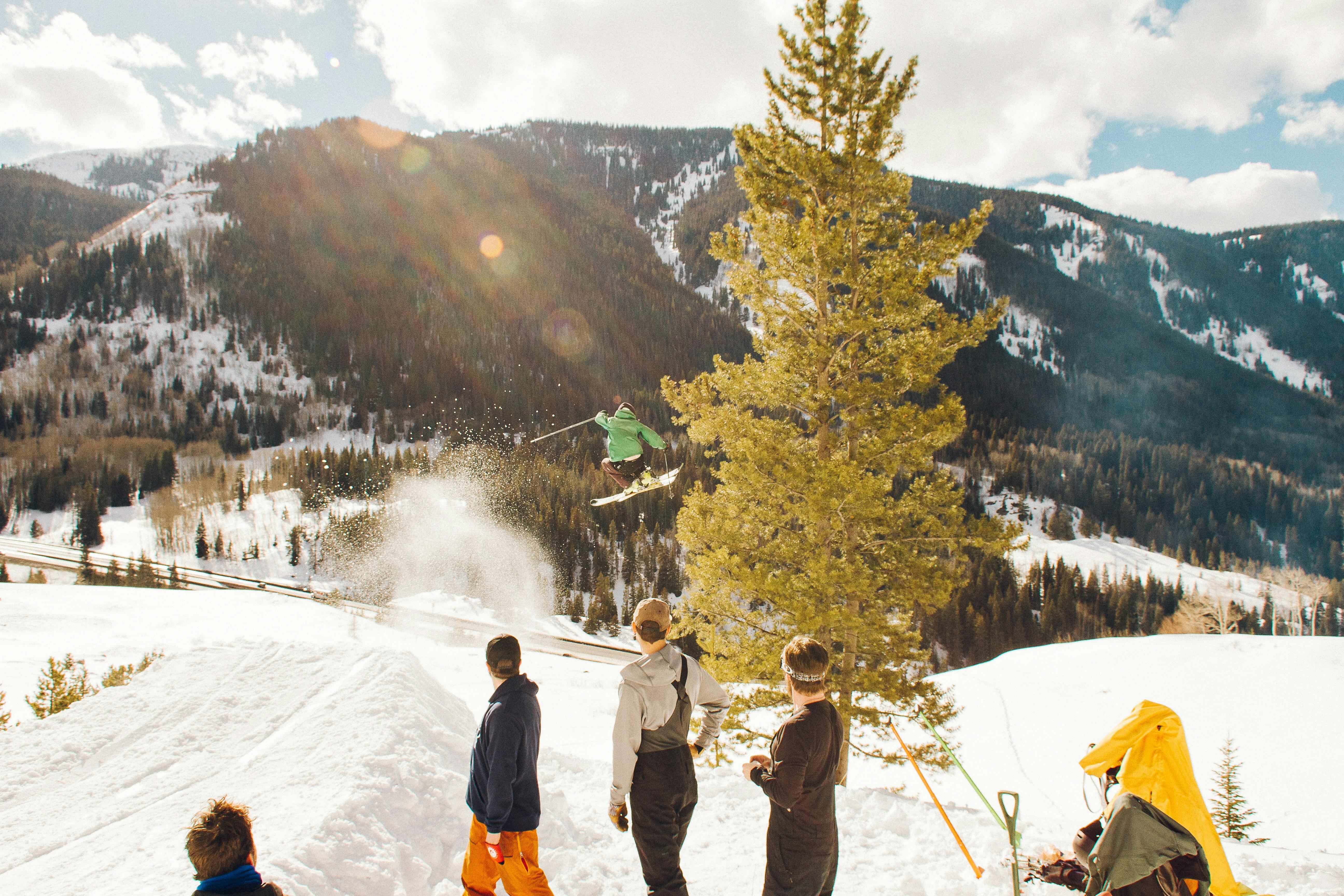 A group of people in long-sleeves and no jackets watch someone jumping on their skis. 
