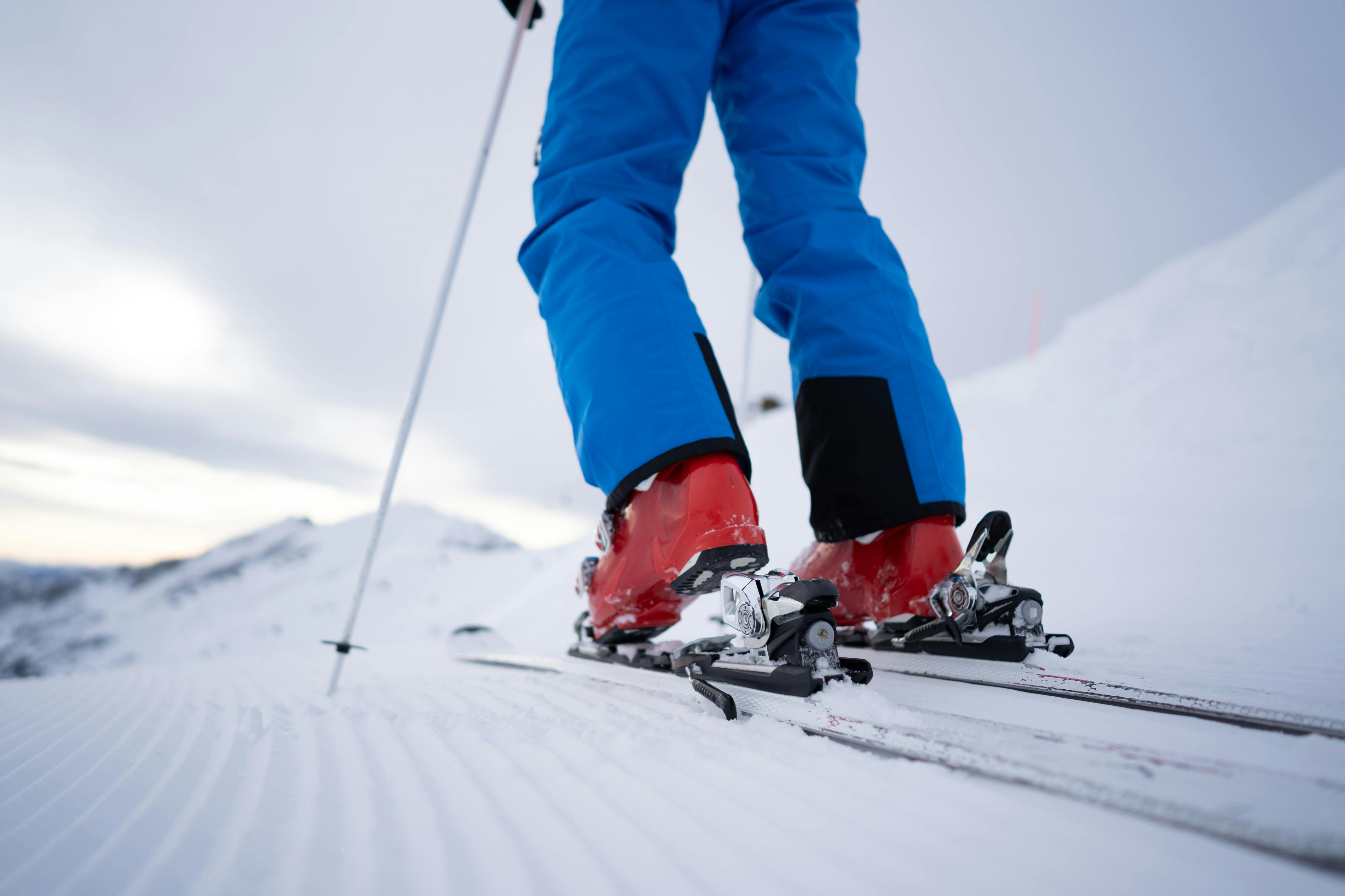A person wearing blue ski pants and red ski boots steps into their binding