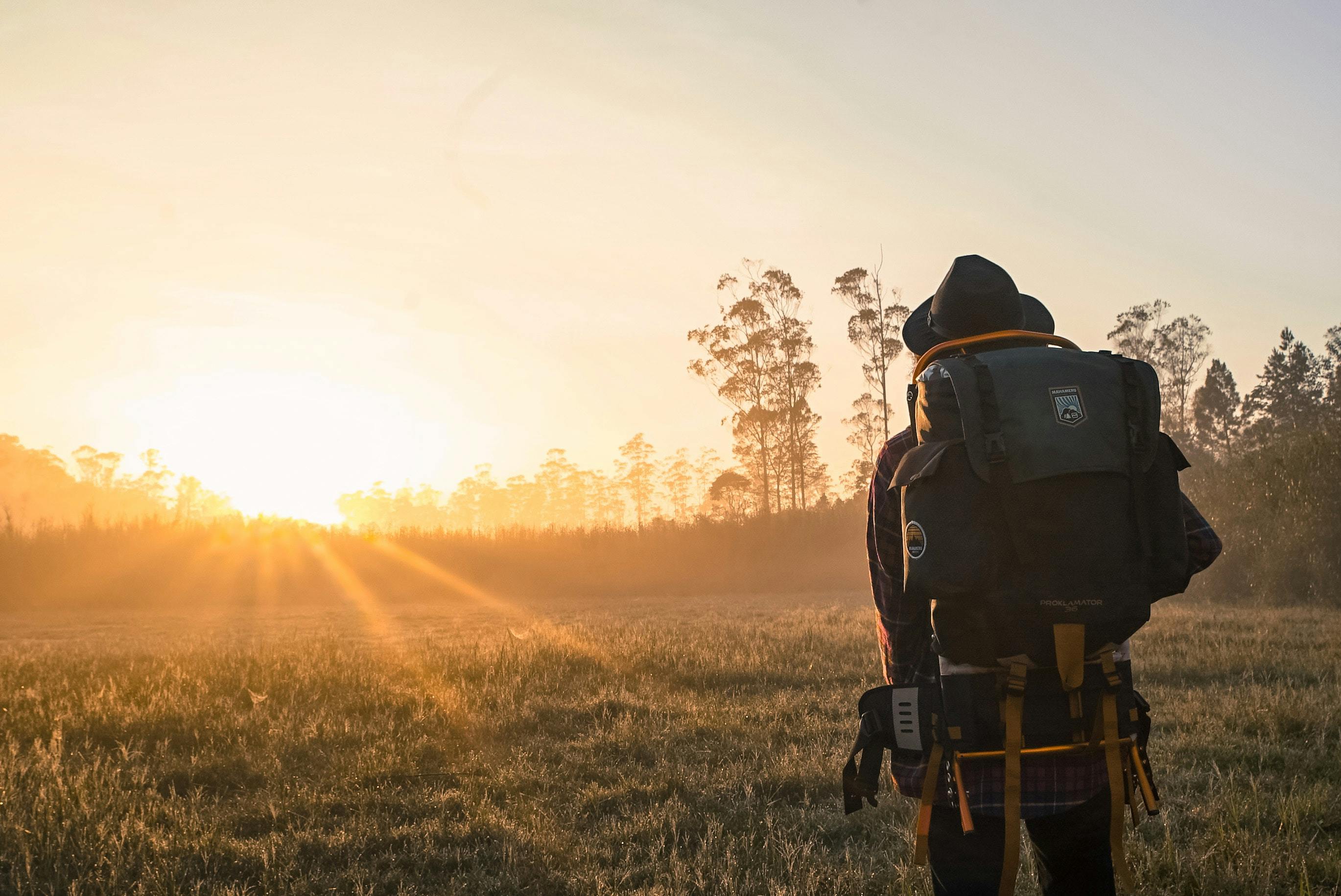 A person in an external-frame backpack looks out at a sunrise