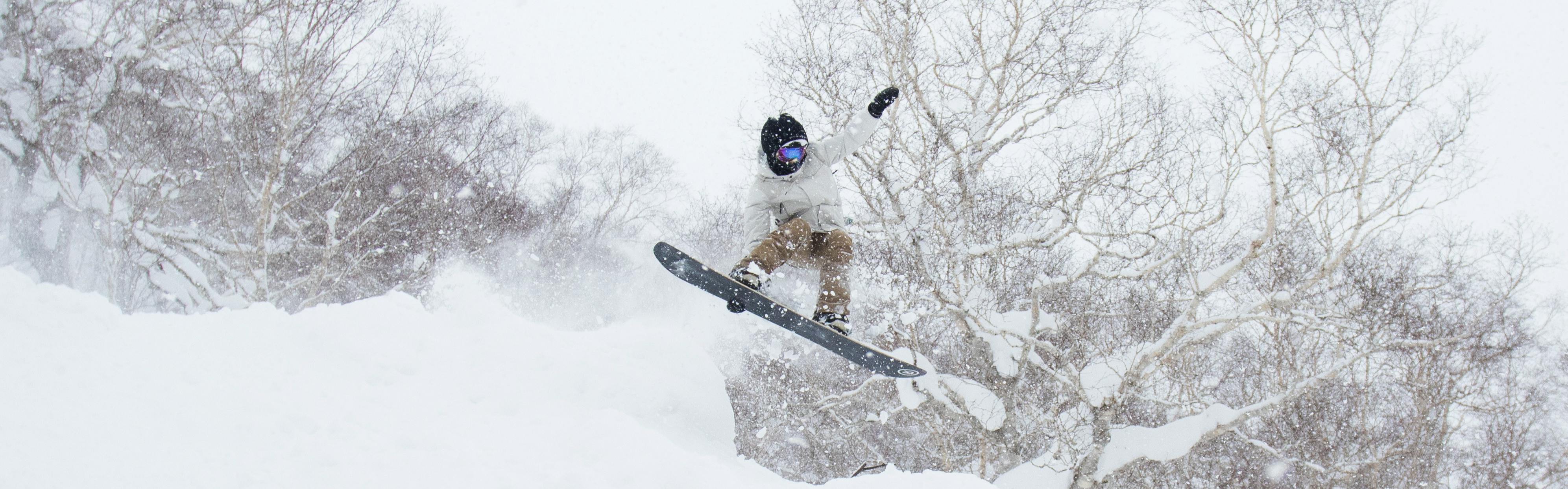 Curated Expert Jesi Scott jumps on her snowboard on a snowy day. 