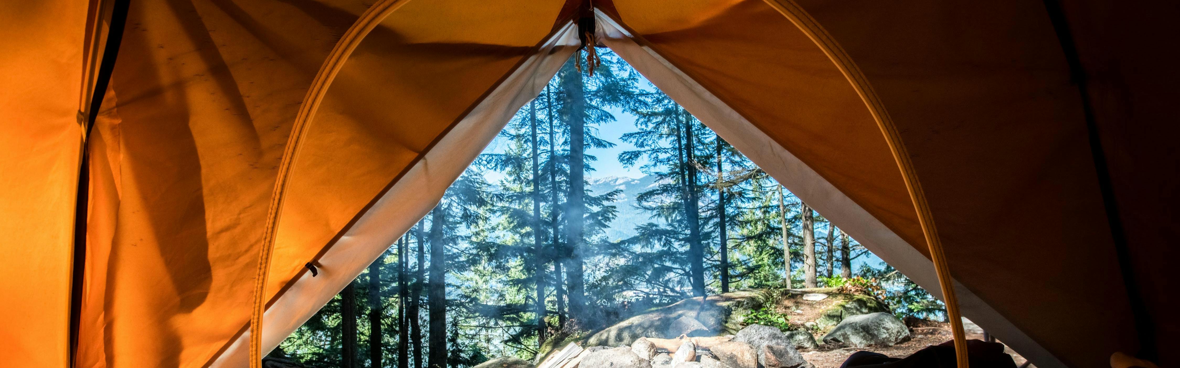 Through the opening of an orange tent, you can see pine trees and blue skies through them.