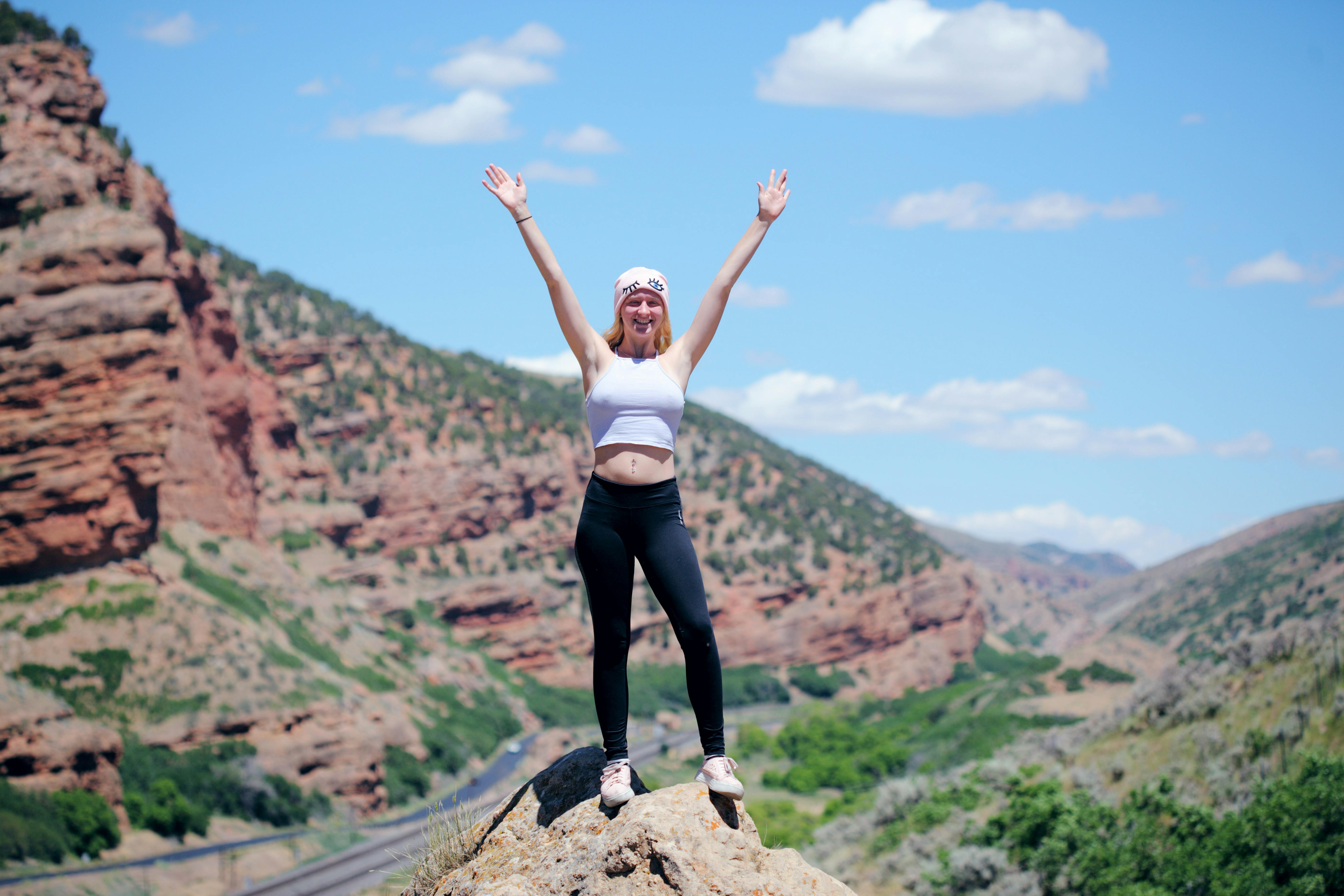 A woman standing at the top of a rock with her hands up and smiling. 