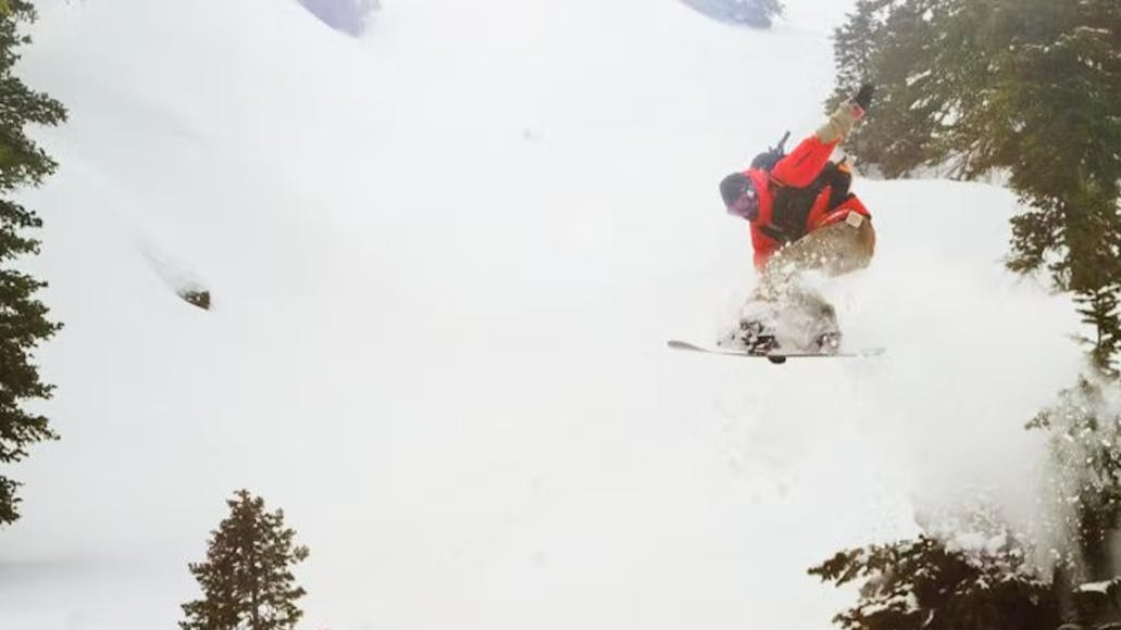 A snowboarder jumping through a powdery area of trees.