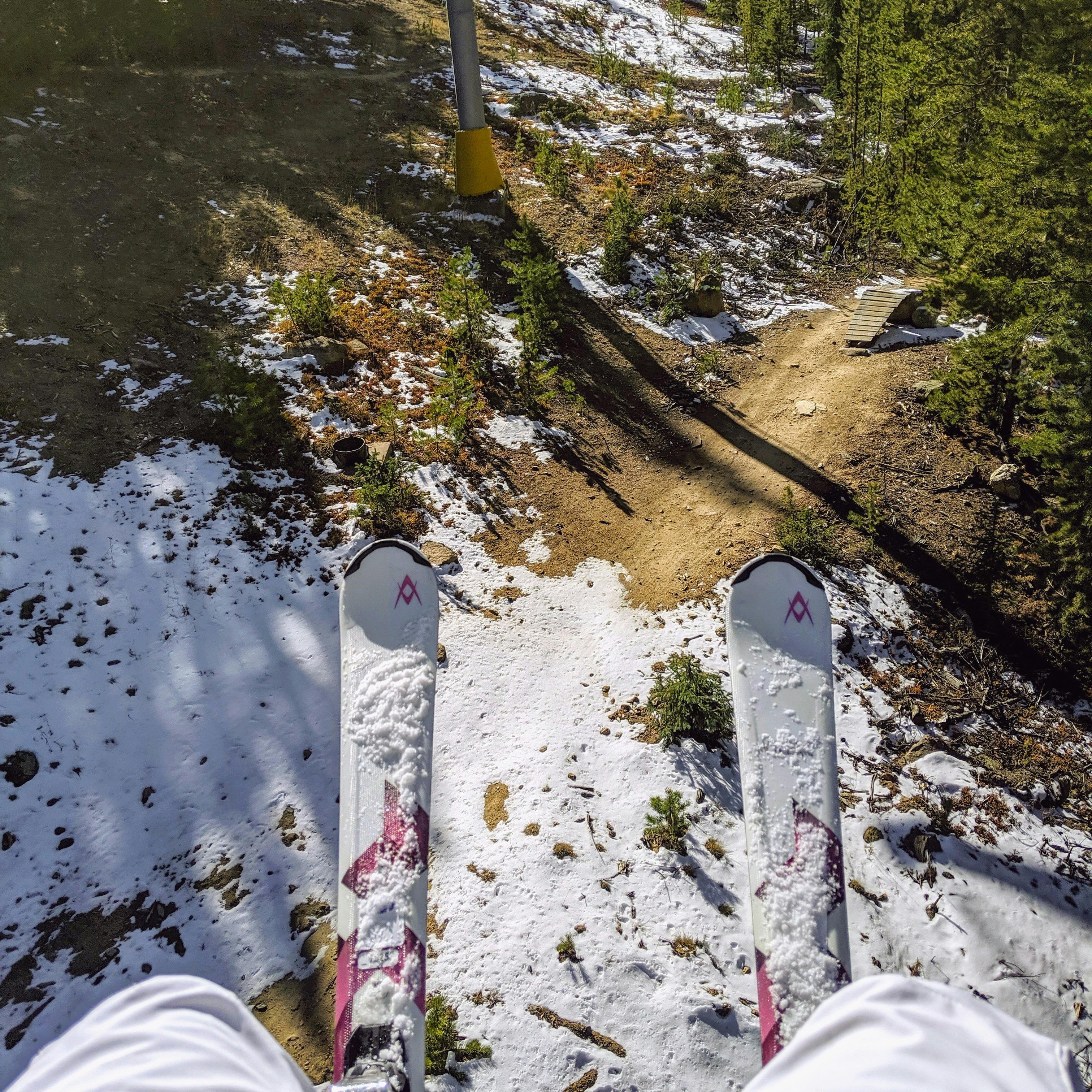 Top down view of a pair of skis as seen from a chairlift above a snowy/dirty ski trail. 