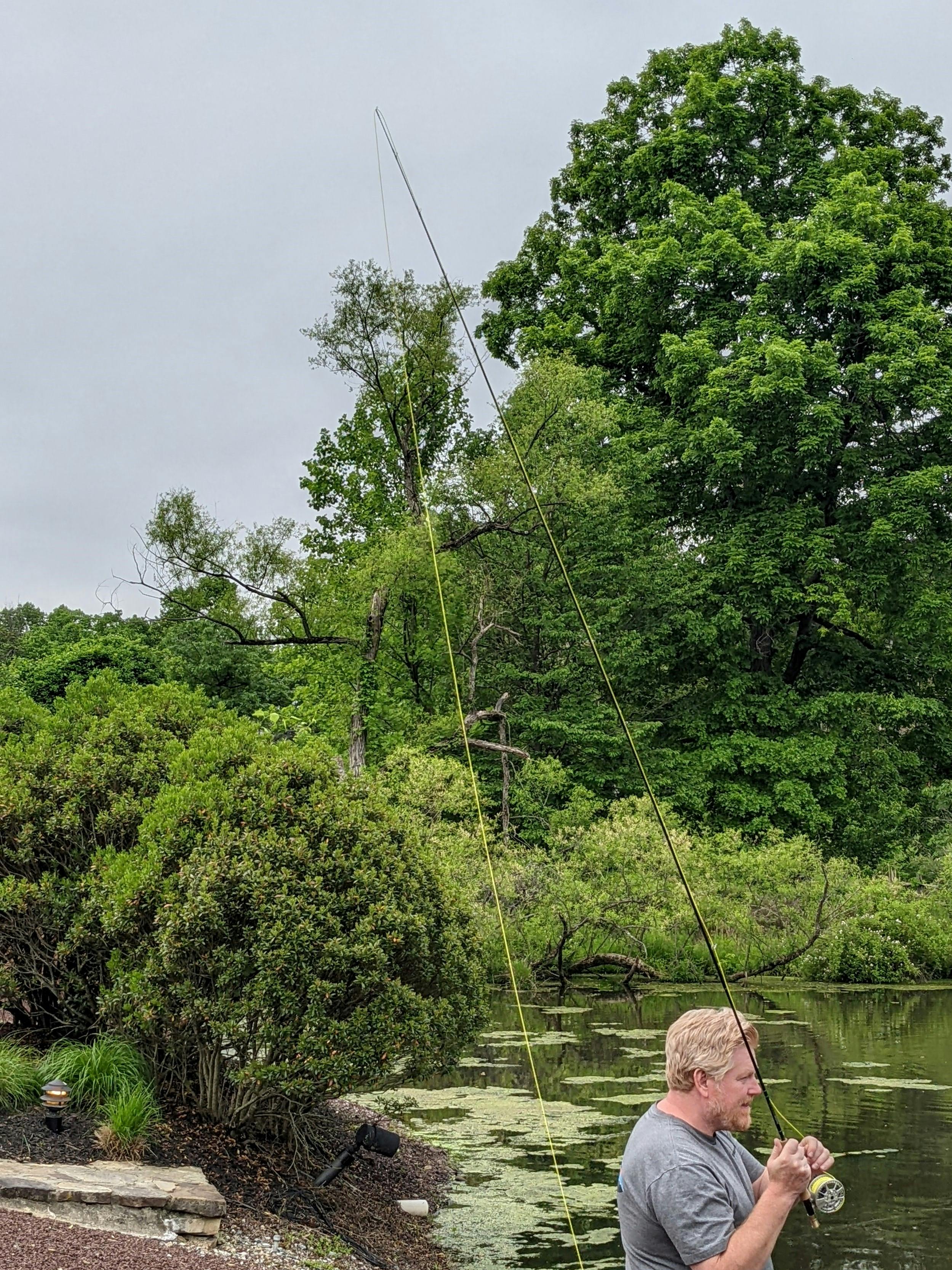 A man gets ready to do a roll cast with a fly rod near a body of water.