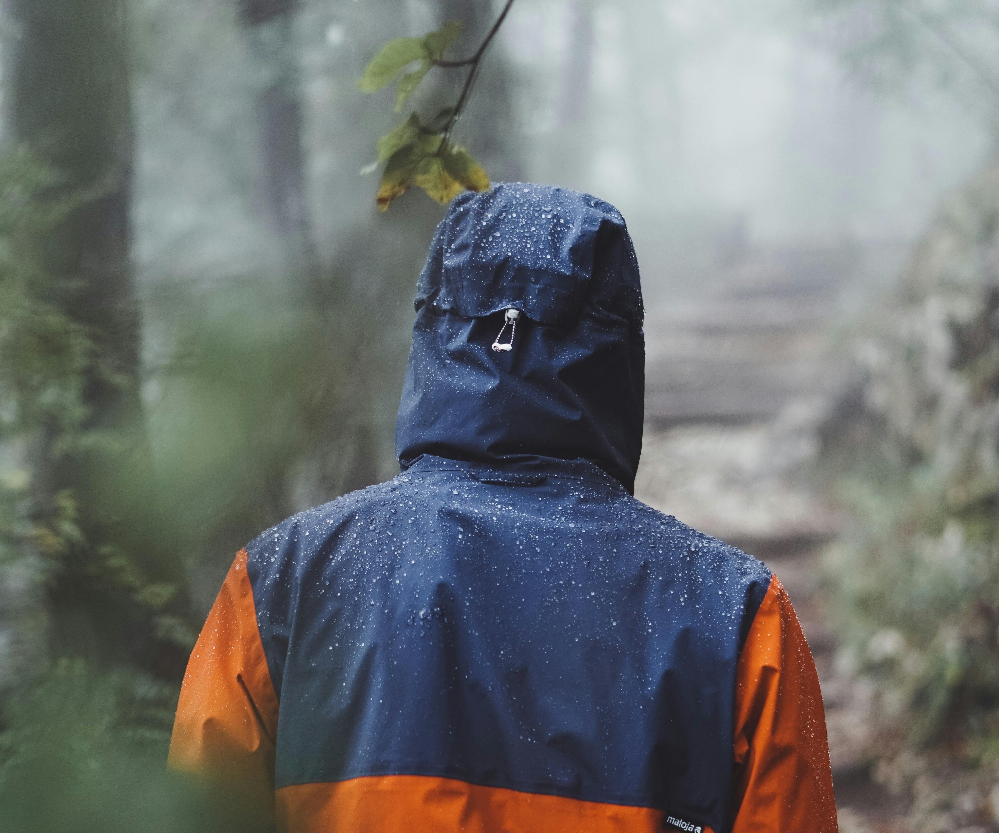 A man wearing a raincoat stands with his back to the camera. 