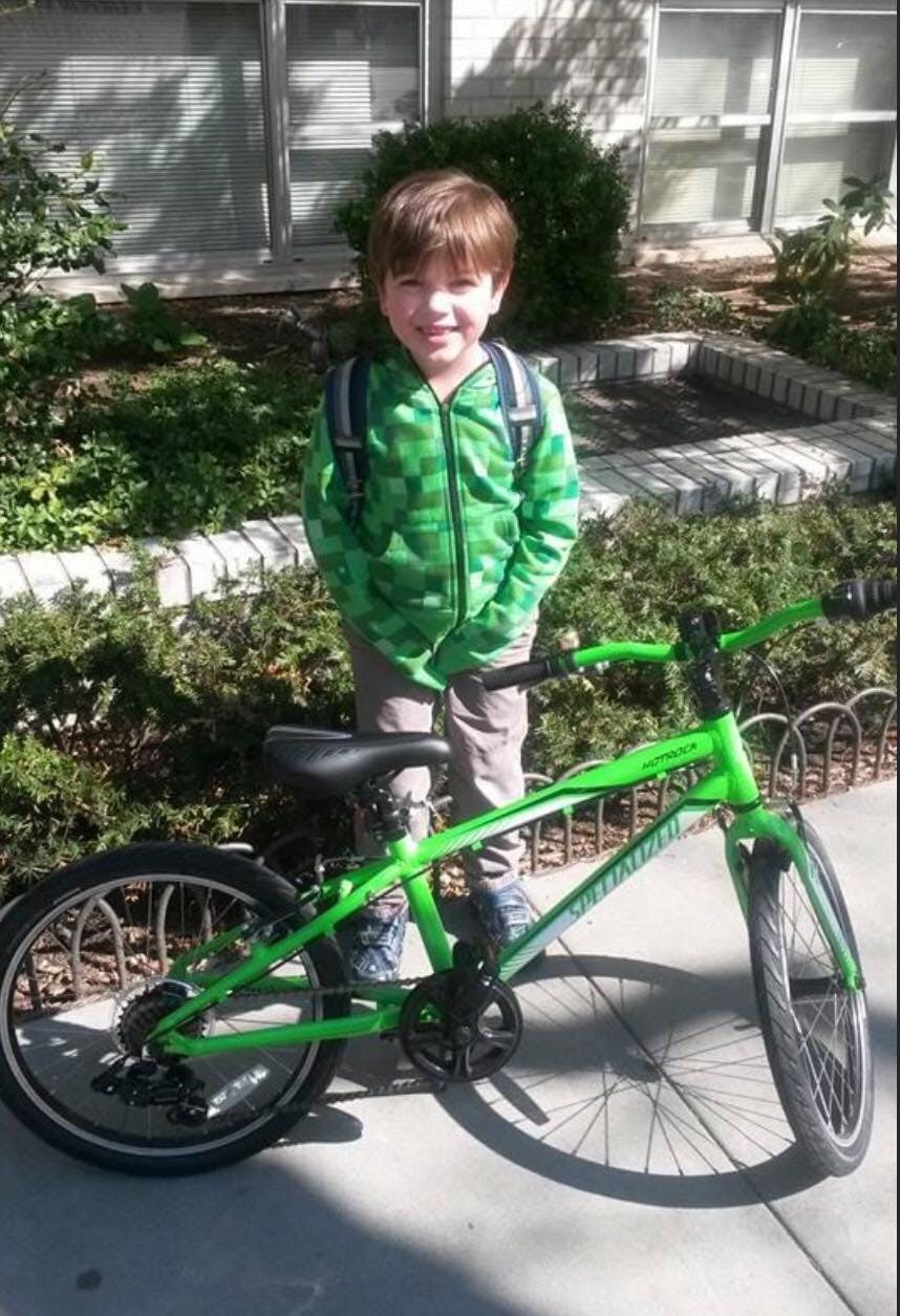 A smiling child with a green bike.