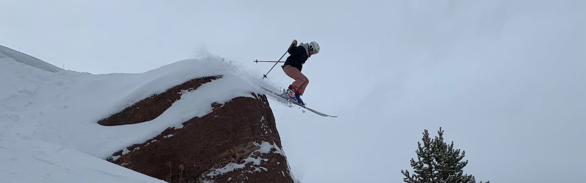 A skier jumping off of a snowy rock. 