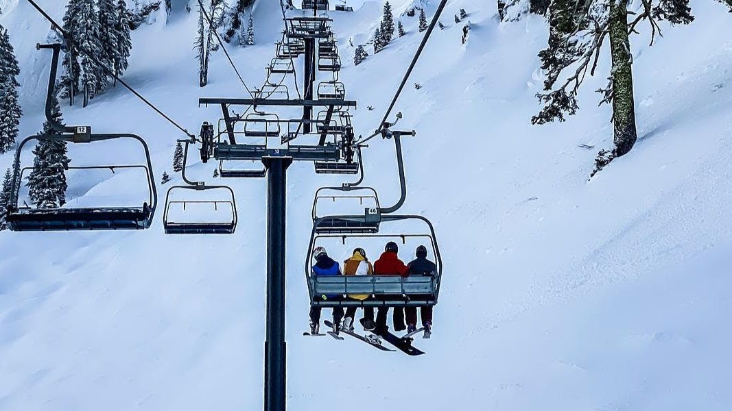 Snowboarders and skier sit on a chairlift.