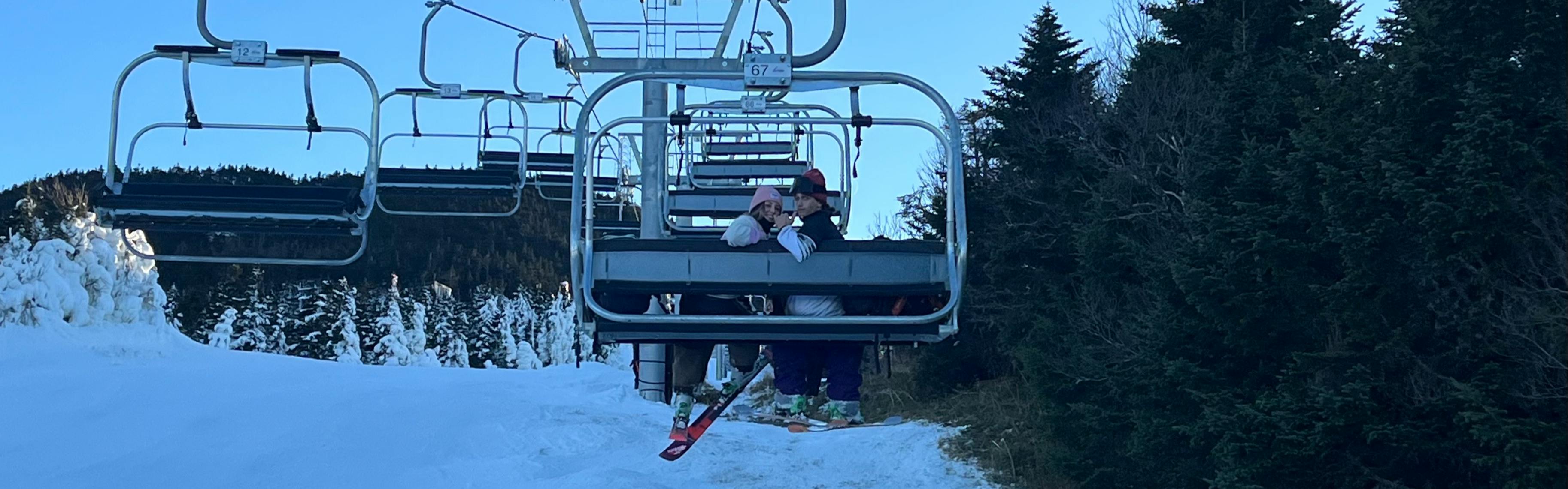 Two people look behind them and smile for the camera while on a chairlift in skis. 