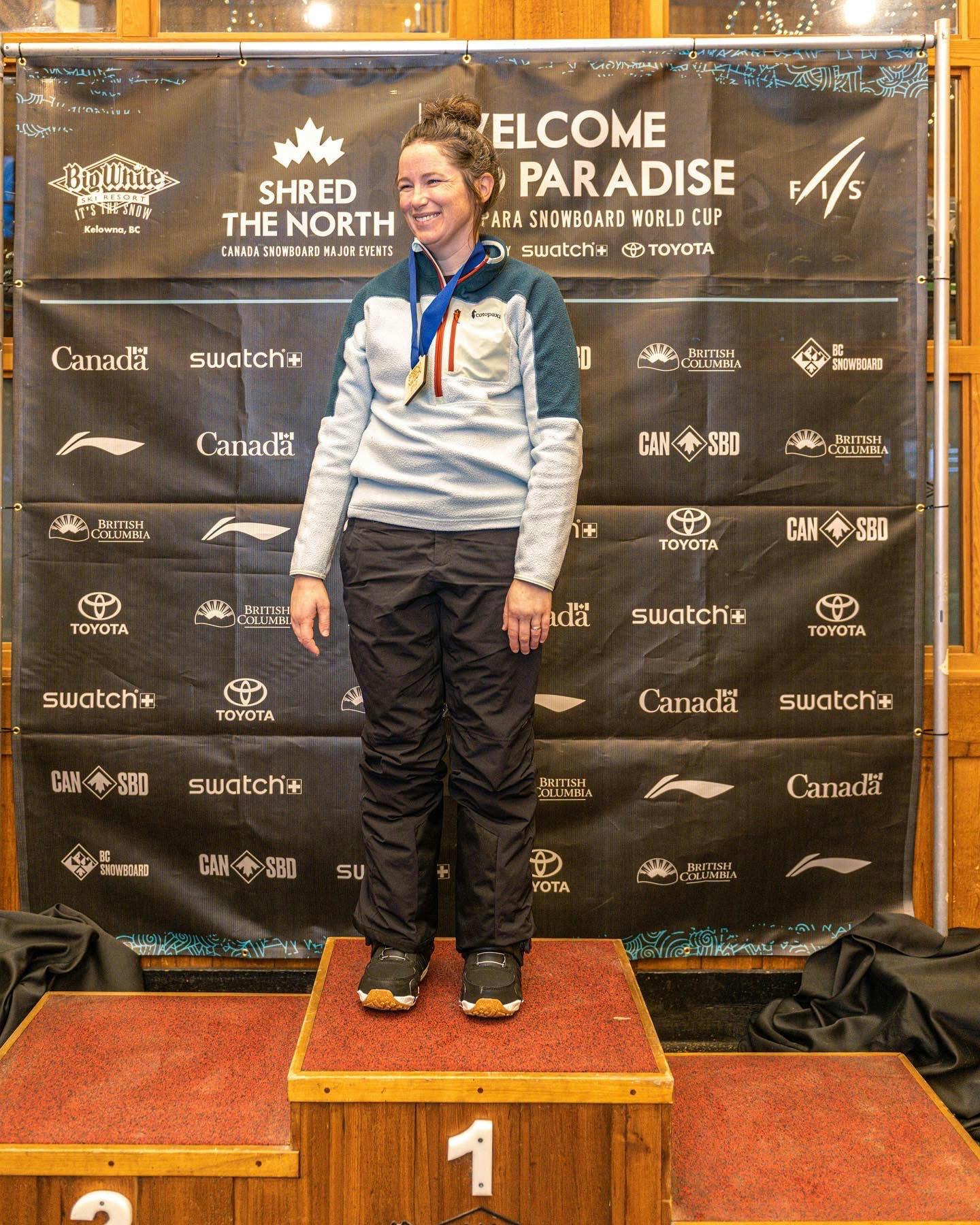Caucasian woman with dark hair standing on a wooden 1st place podium with a medal around her neck and the Burton Felix StepOns boots.