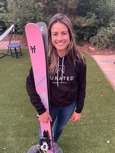 A woman stands smiling holding her skis.
