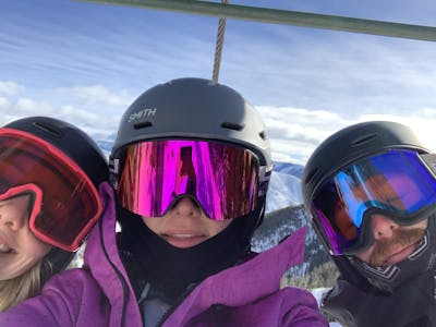 Three skiers wearing helmets and goggles on a chairlift at a ski resort. 