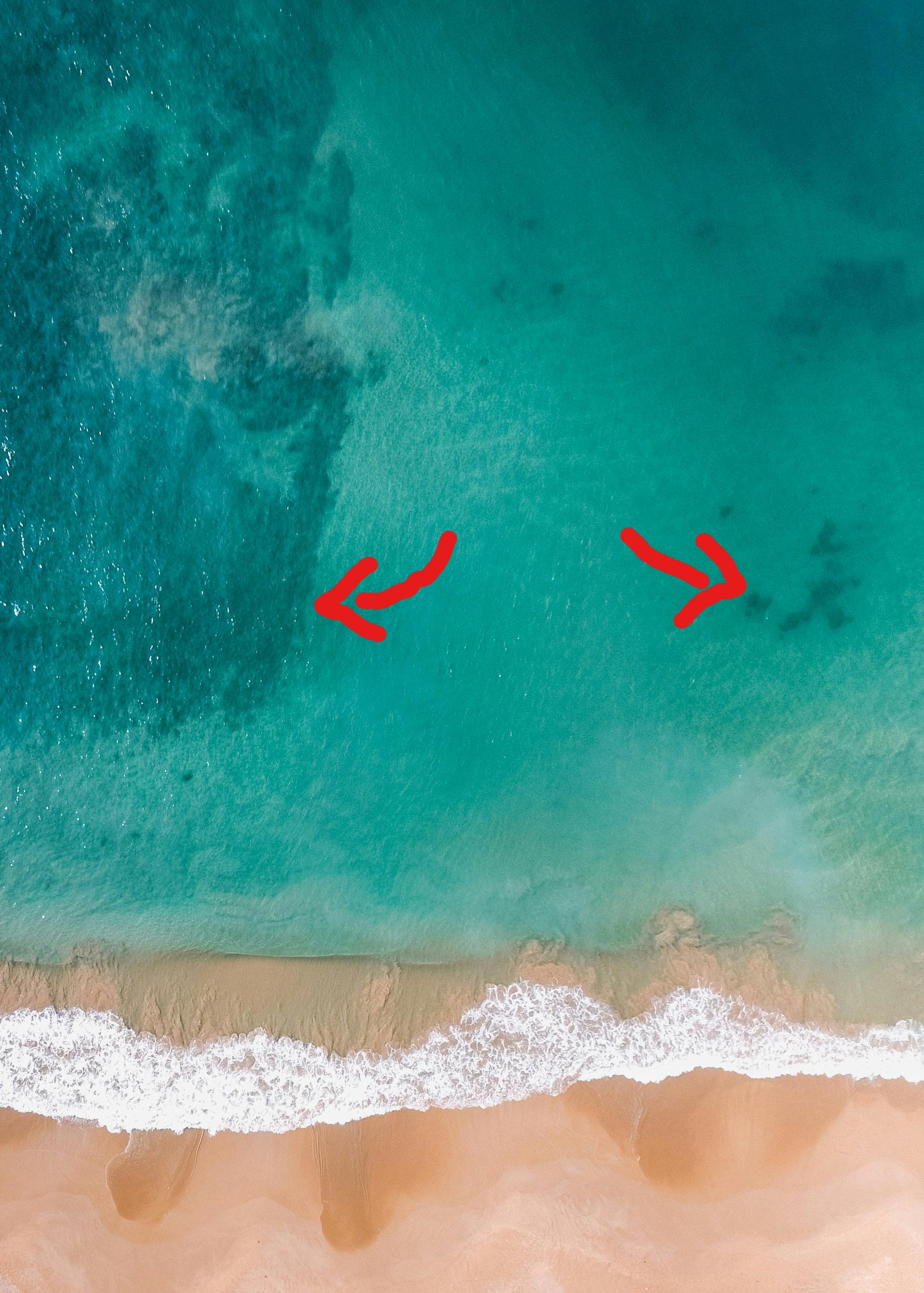 An aerial view of the ocean shore with arrows pointing to a reef on either side. 