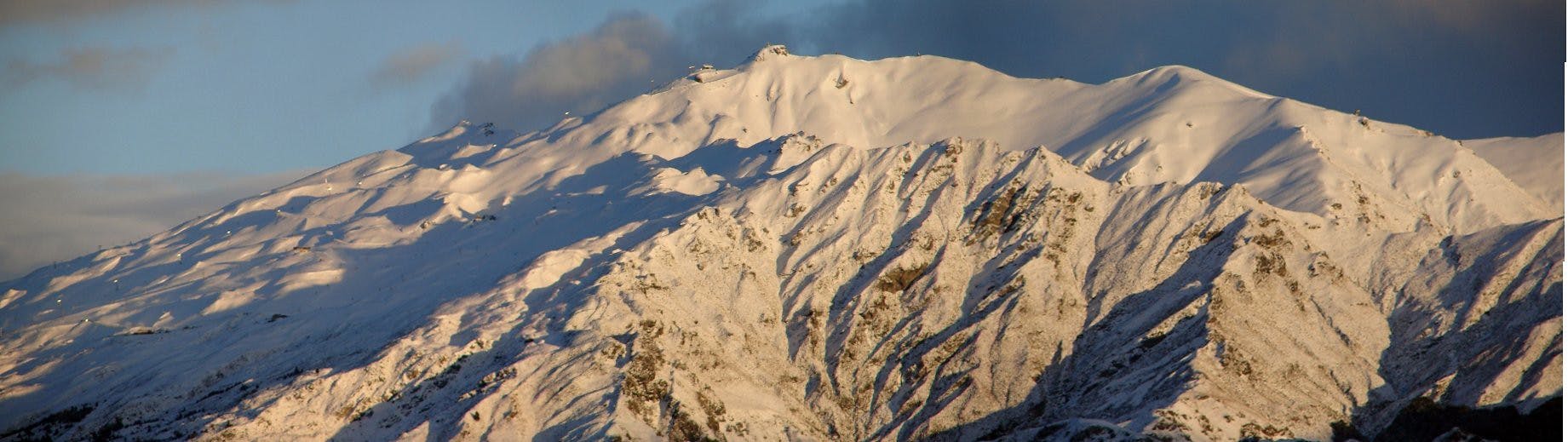 A snowy peak with clouds coming off of it. 