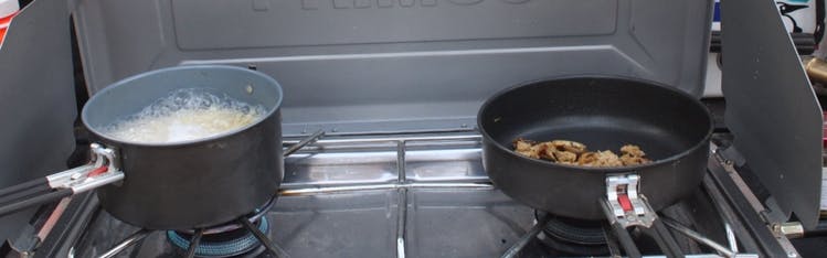 A pot and a pan on a cooking stove. There is something boiling in the pot. 