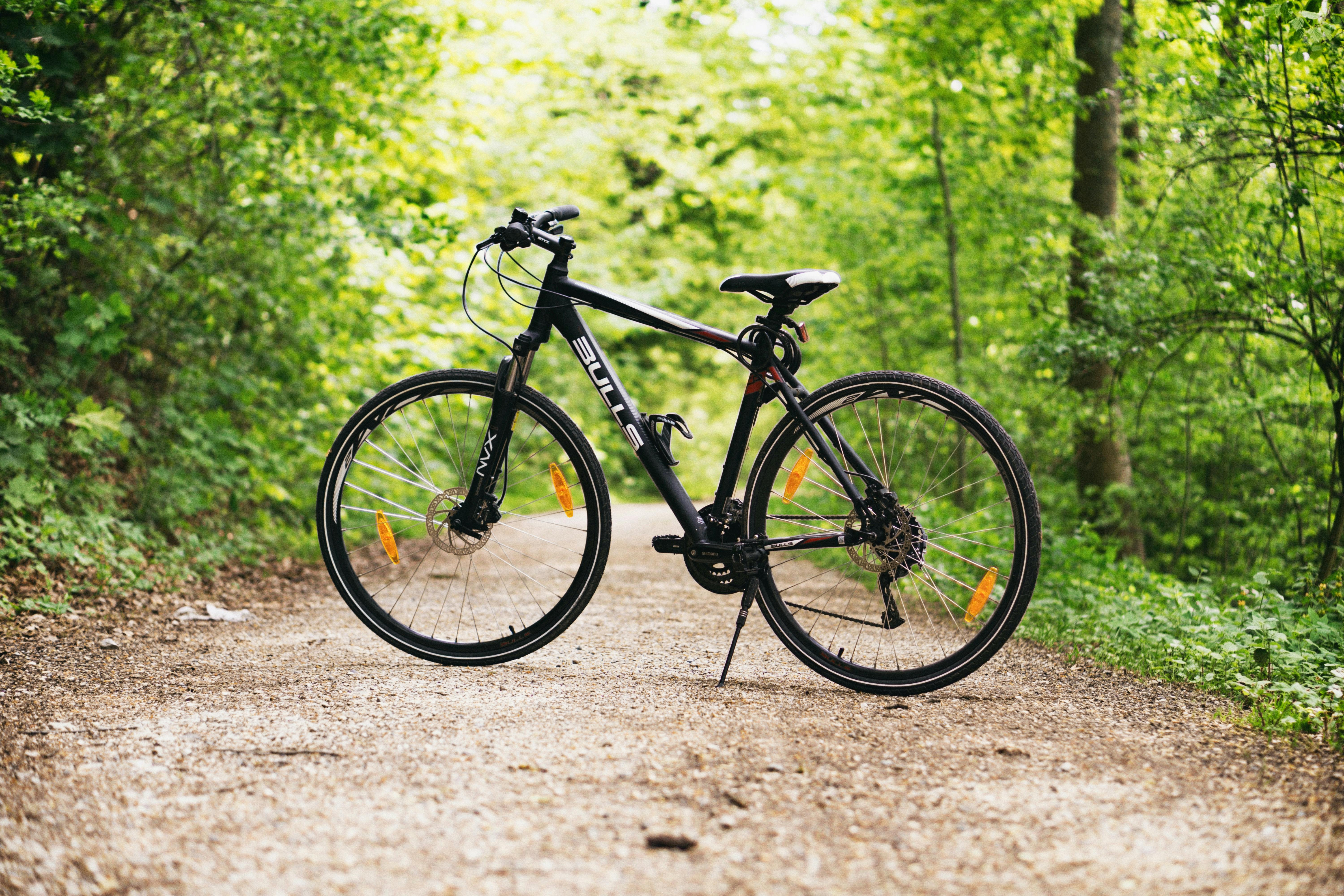 A black hybrid bicycle sits alone on a dirt path in a wooded area