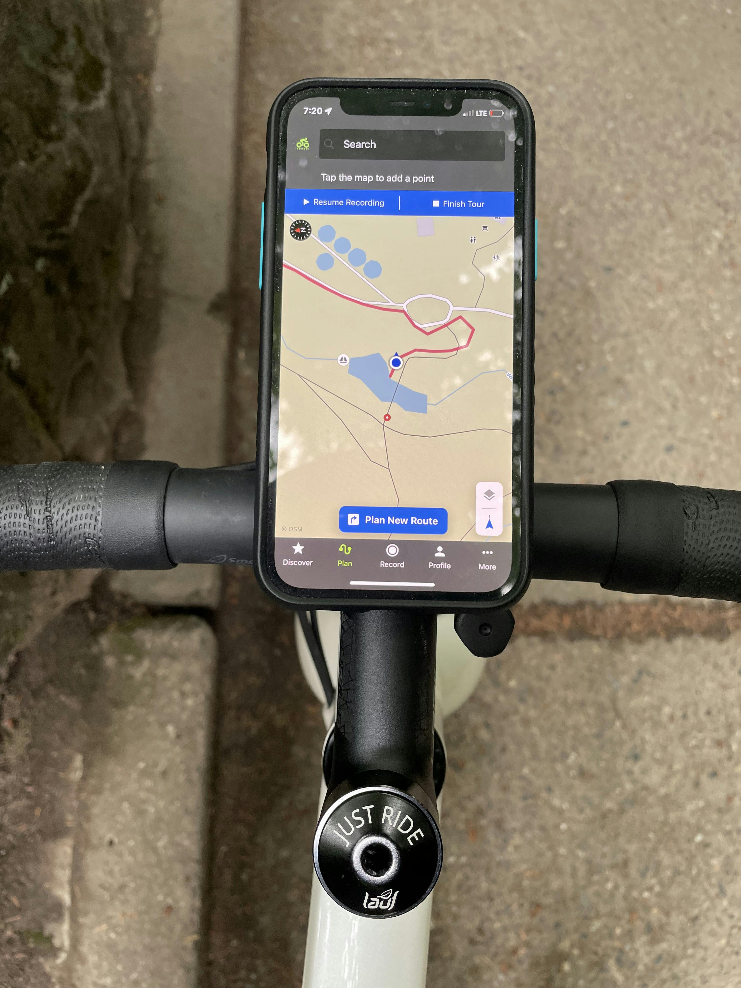 A smartphone mounted to handlebars on a bike. There is a map visible on the screen of the smartphone. 