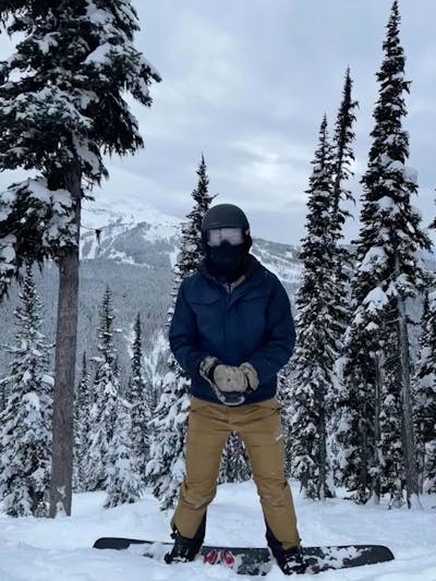 A snowboarder standing in a snowy tree area. 