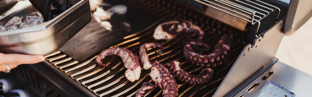 Someone lays some octopus on a grill. 