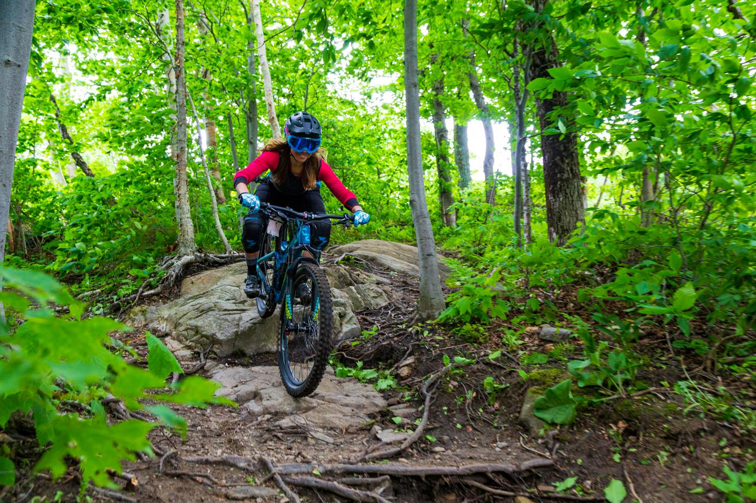 Liv Cycling Senior Product Marketing Specialist Jen Audia mountain biking through a bright, leafy green forest.