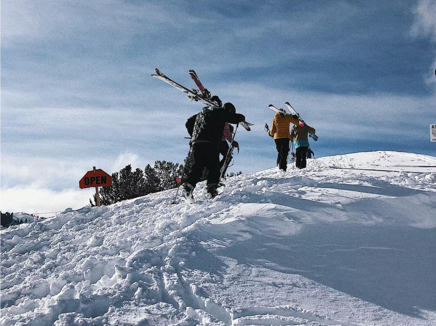 Four skiers walking along a ridge holding their skis. 