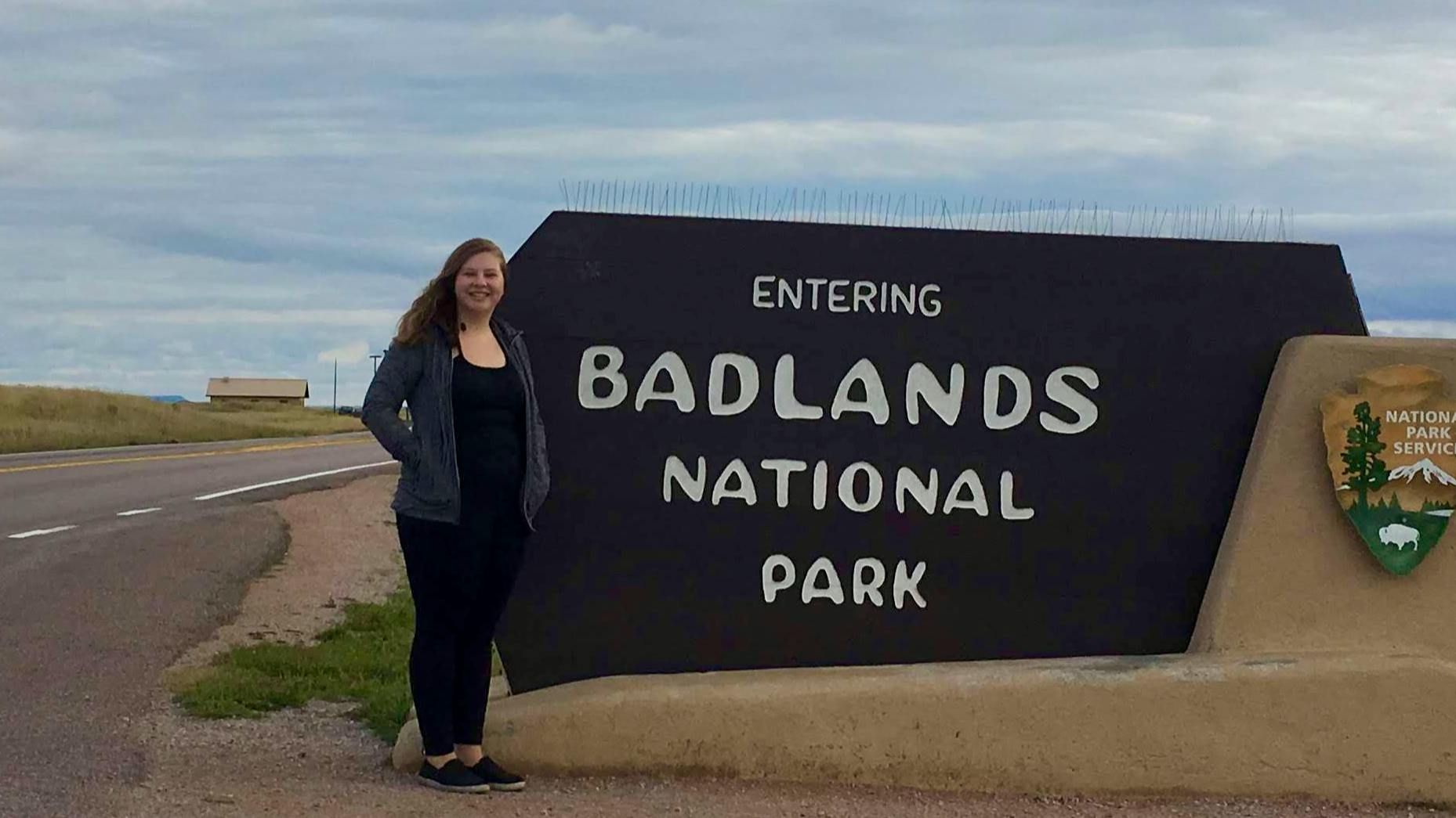 The author stands on the side of the road next to a National Park Service sign that reads Entering Badlands National Park. 