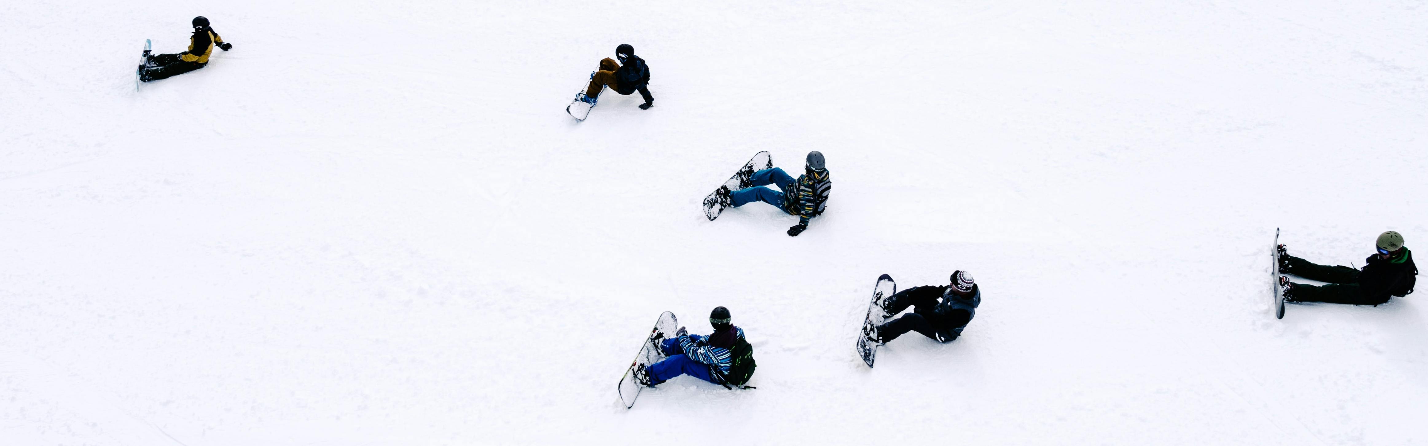 Six snowboarders sit on the snow, scattered around