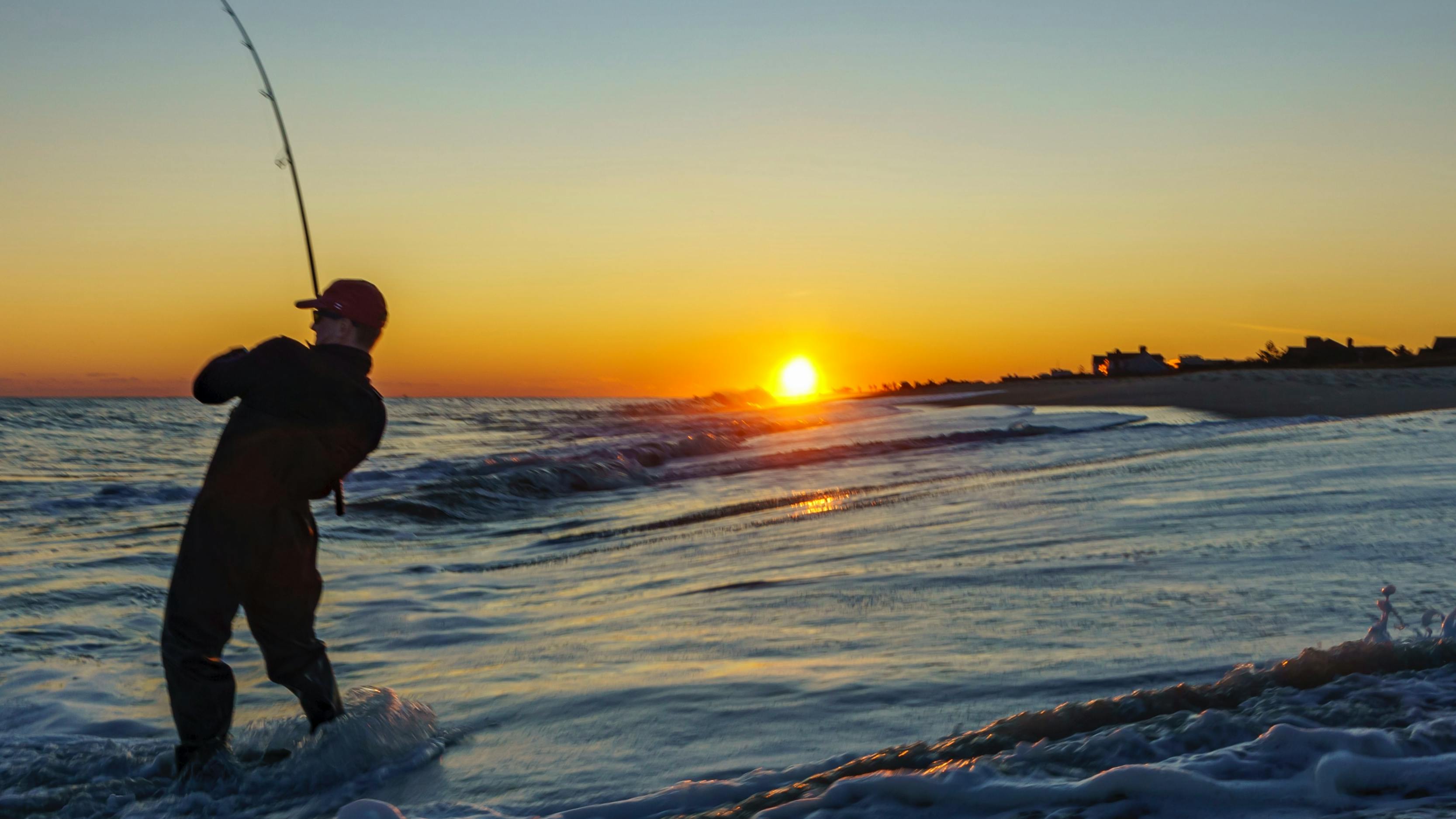 A man fishing in an ocean as the sun sets. 
