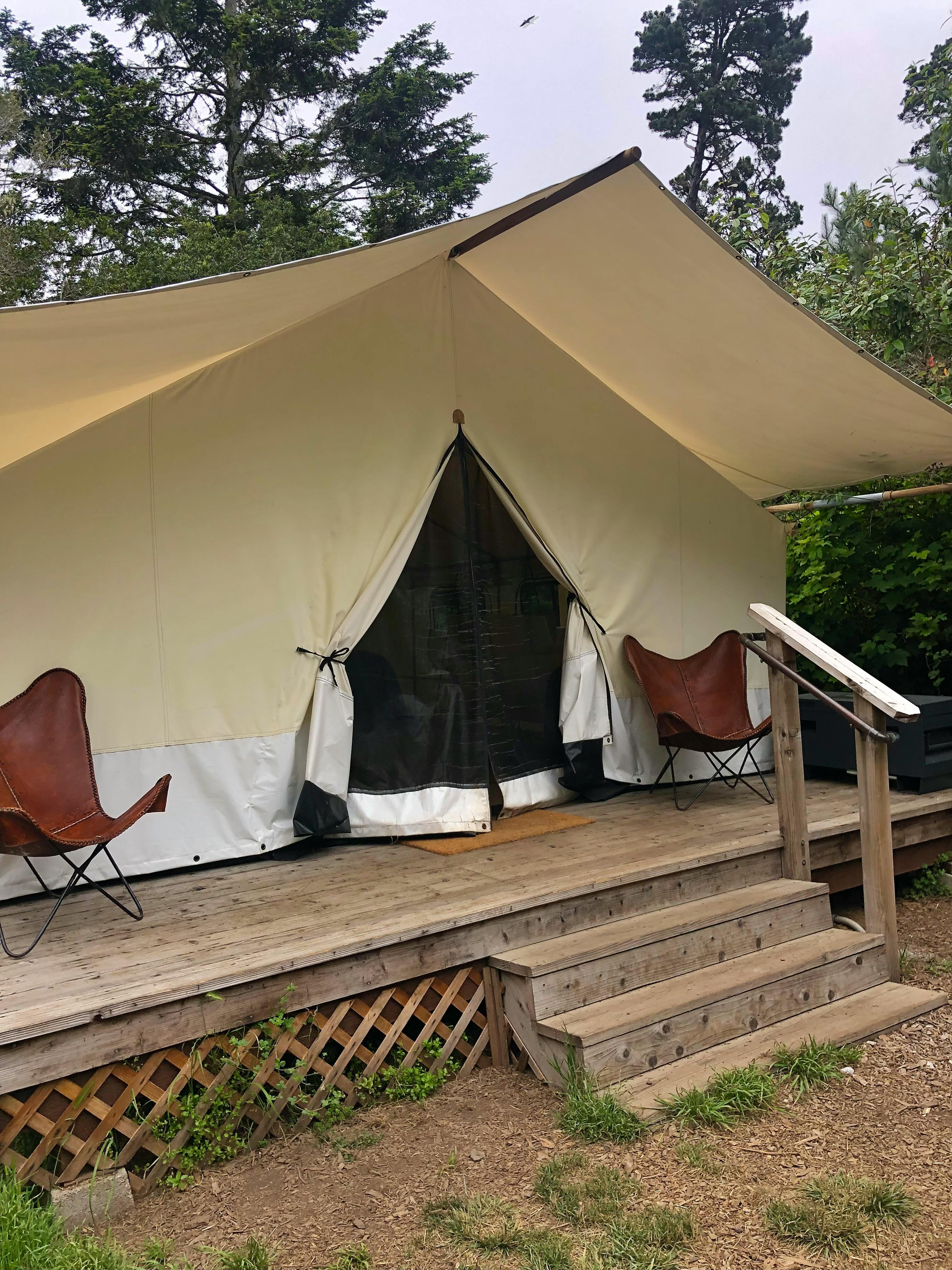 A large canvas tent with a deck outside that two leather chairs sit on. 