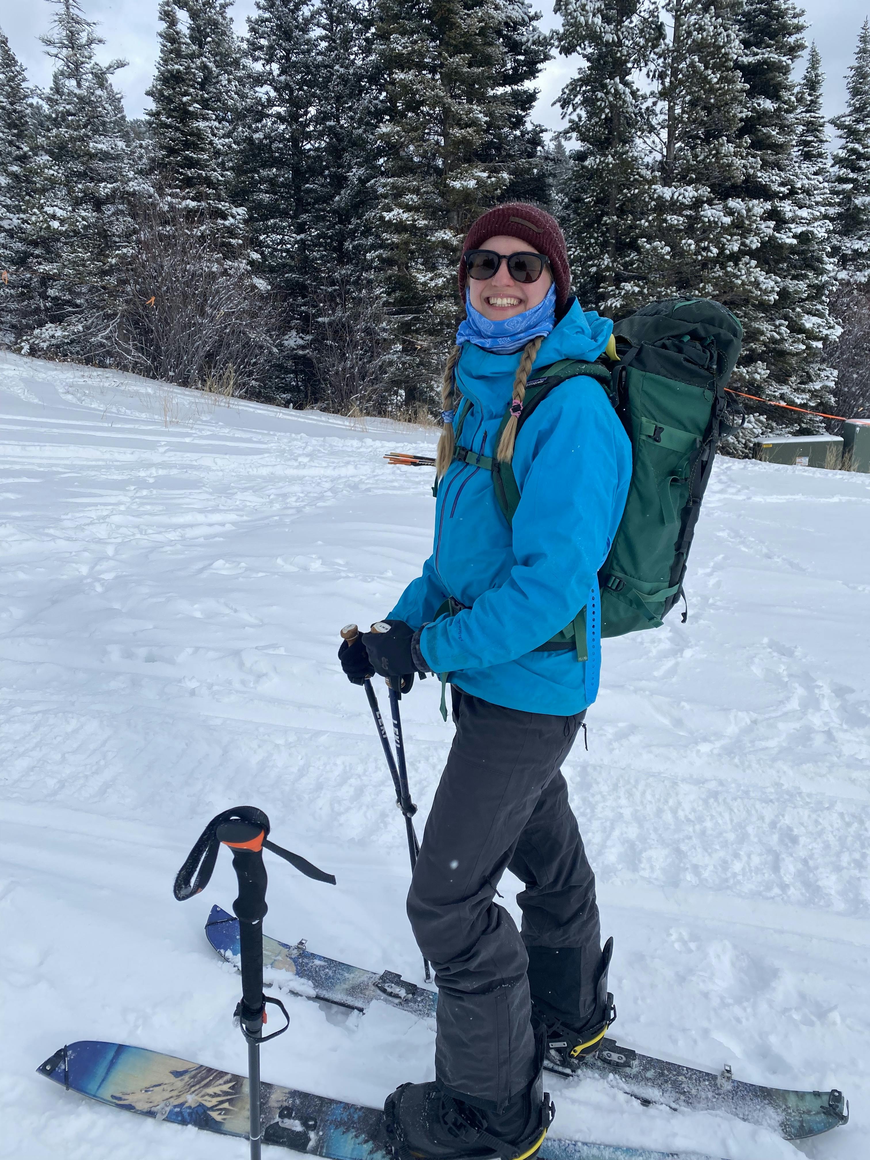 A woman splitboarding on a snowy trail. Her splitboard is in uphill mode and she is wearing a backpack.