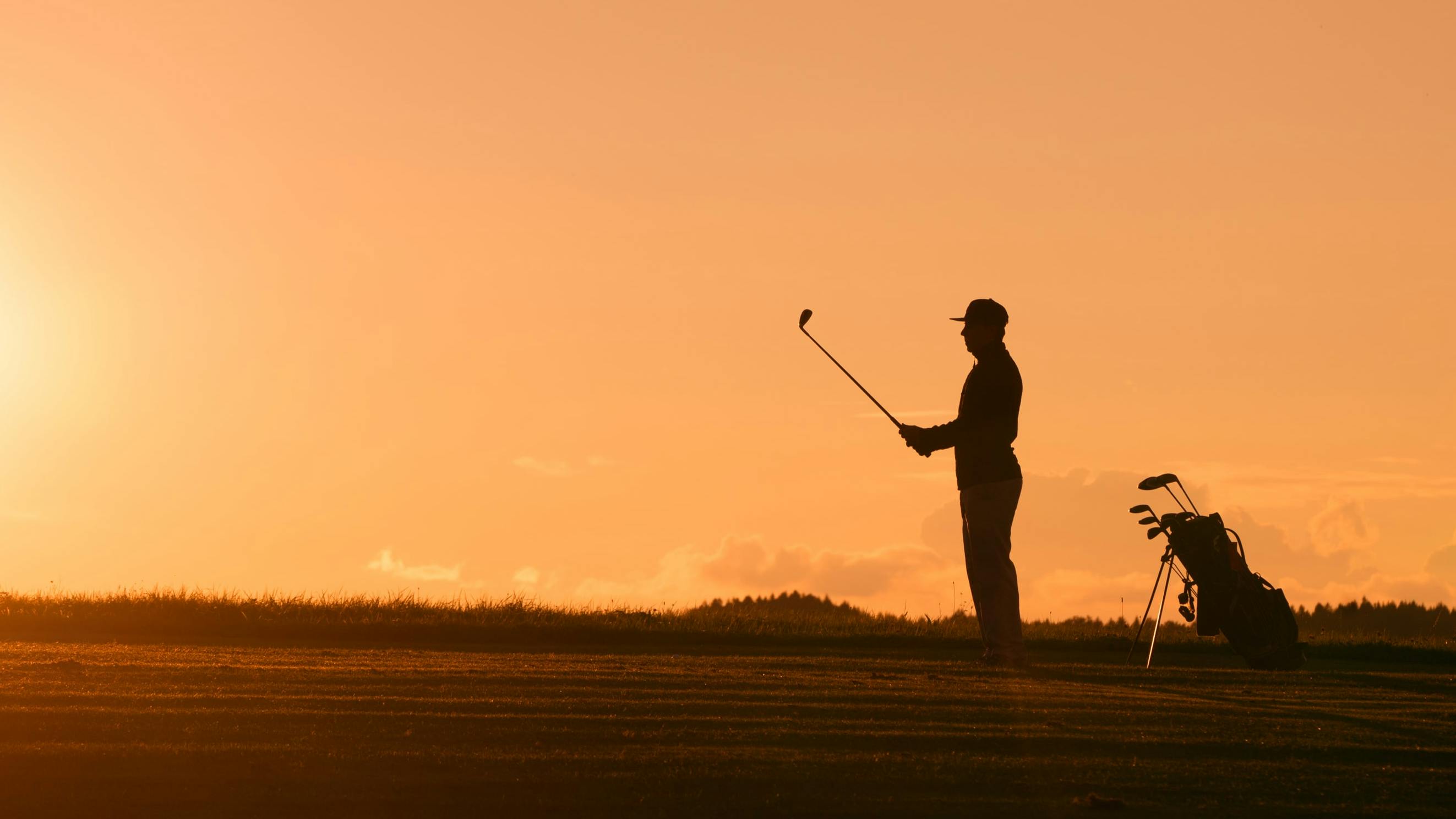 A golfer stands against a sunset