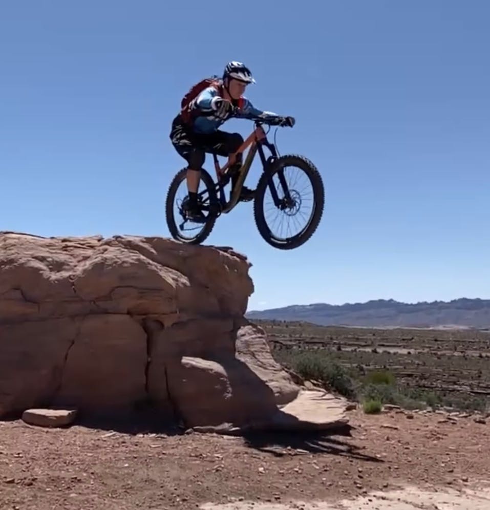 A mountain biker on the Rocky Mountain Altitude Carbon 50 Mountain Bike cycling off of a large rock. 