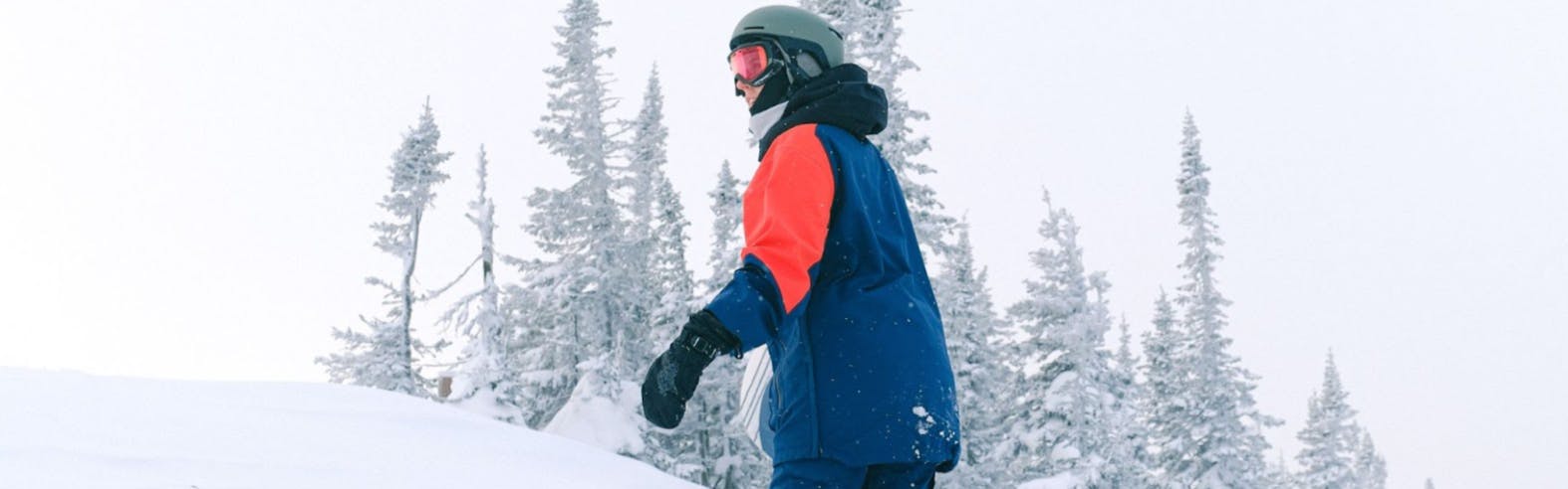 A snowboarder walking uphill with his goggles under his helmet. 