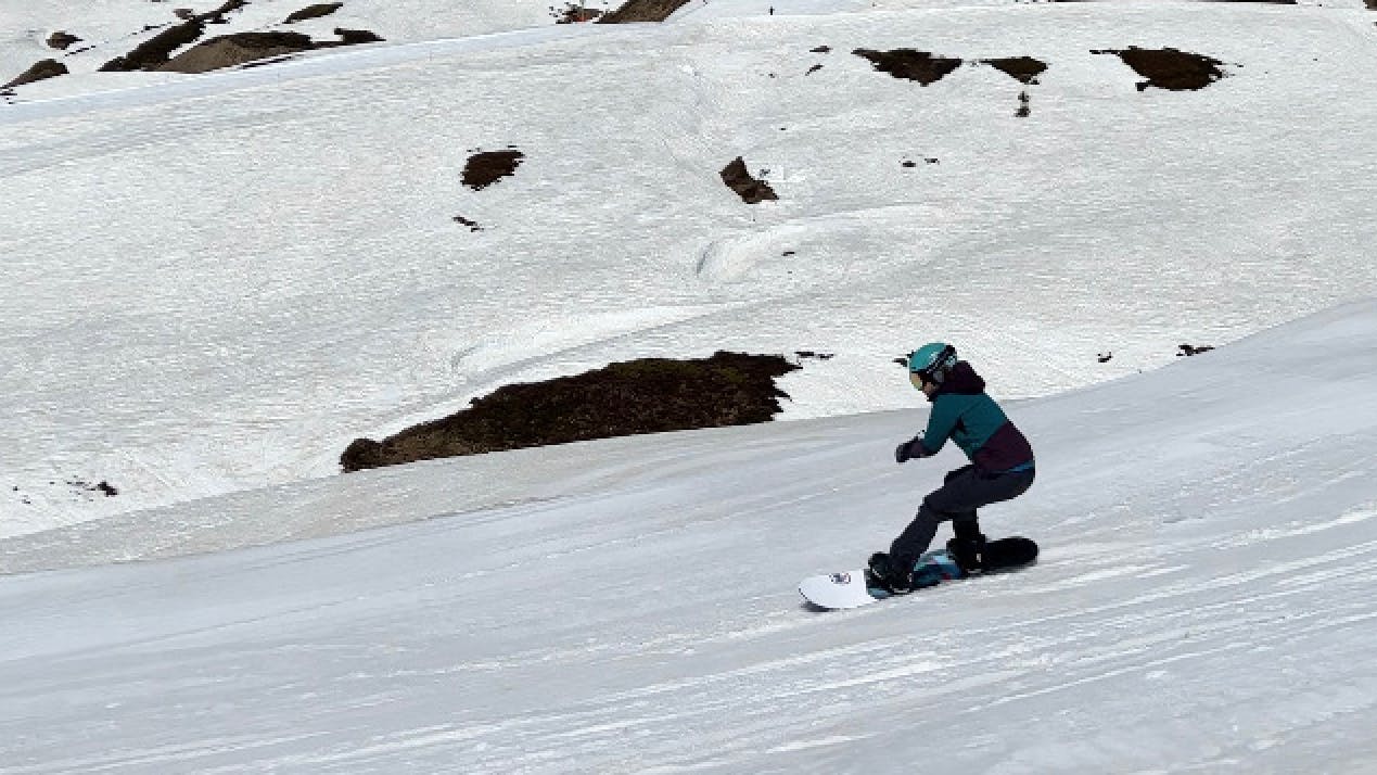 A snowboarder turns down a snowy trail. She is wearing a blue jacket and a blue helmet.