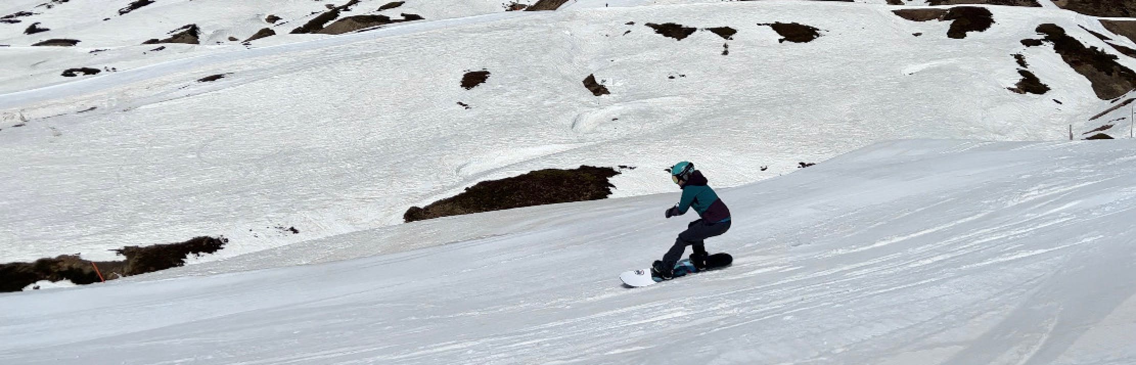 A snowboarder turns down a snowy trail. She is wearing a blue jacket and a blue helmet.
