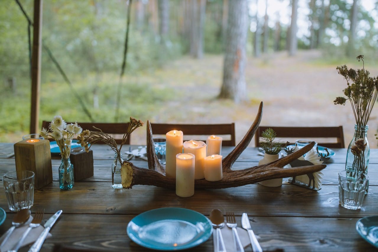 A table with candles and plates and utensils. The table is outside.