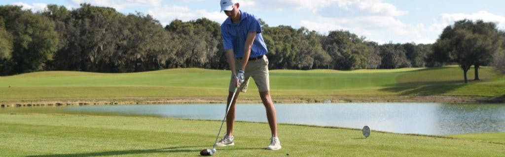 Golfer in blue shirt and shorts teeing the ball up to drive