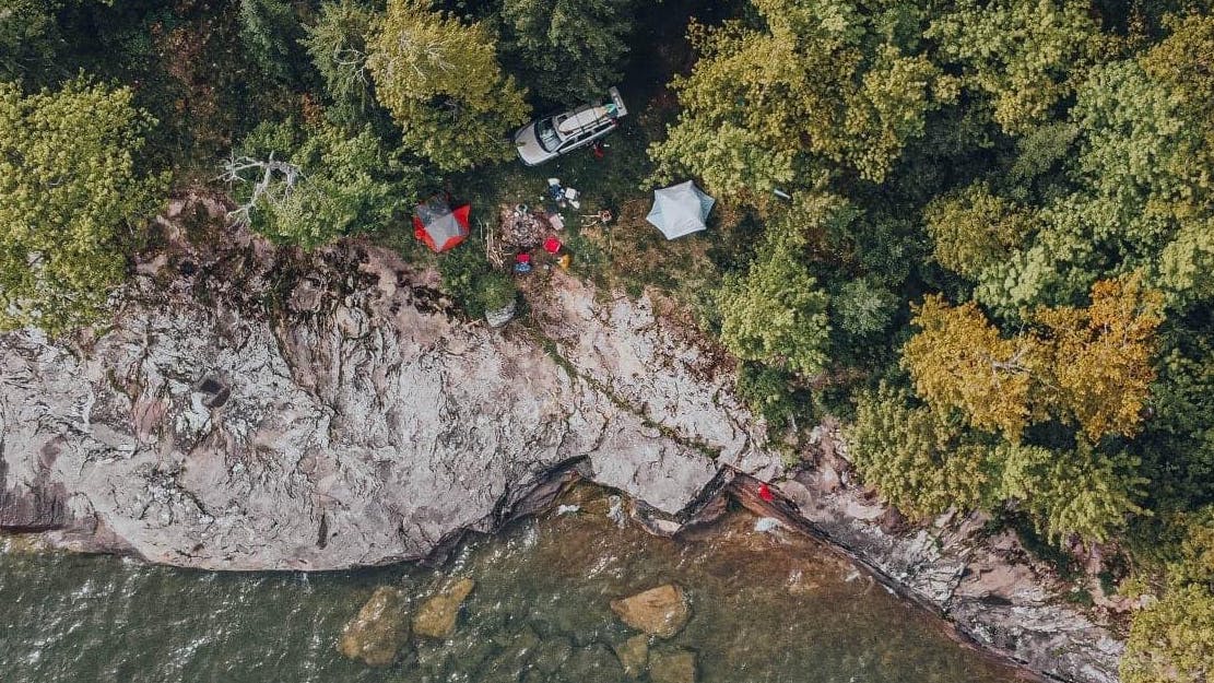 An aerial view of a tent and some campers camping on the edge of some rocks near water. 